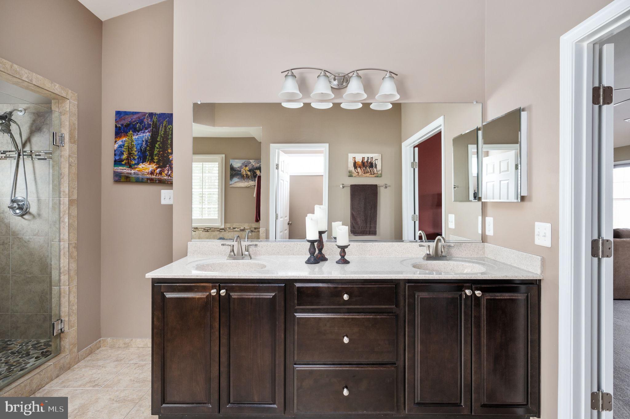 Bathroom with a double-sink dark wood vanity, large mirror, and glass-enclosed tiled shower.