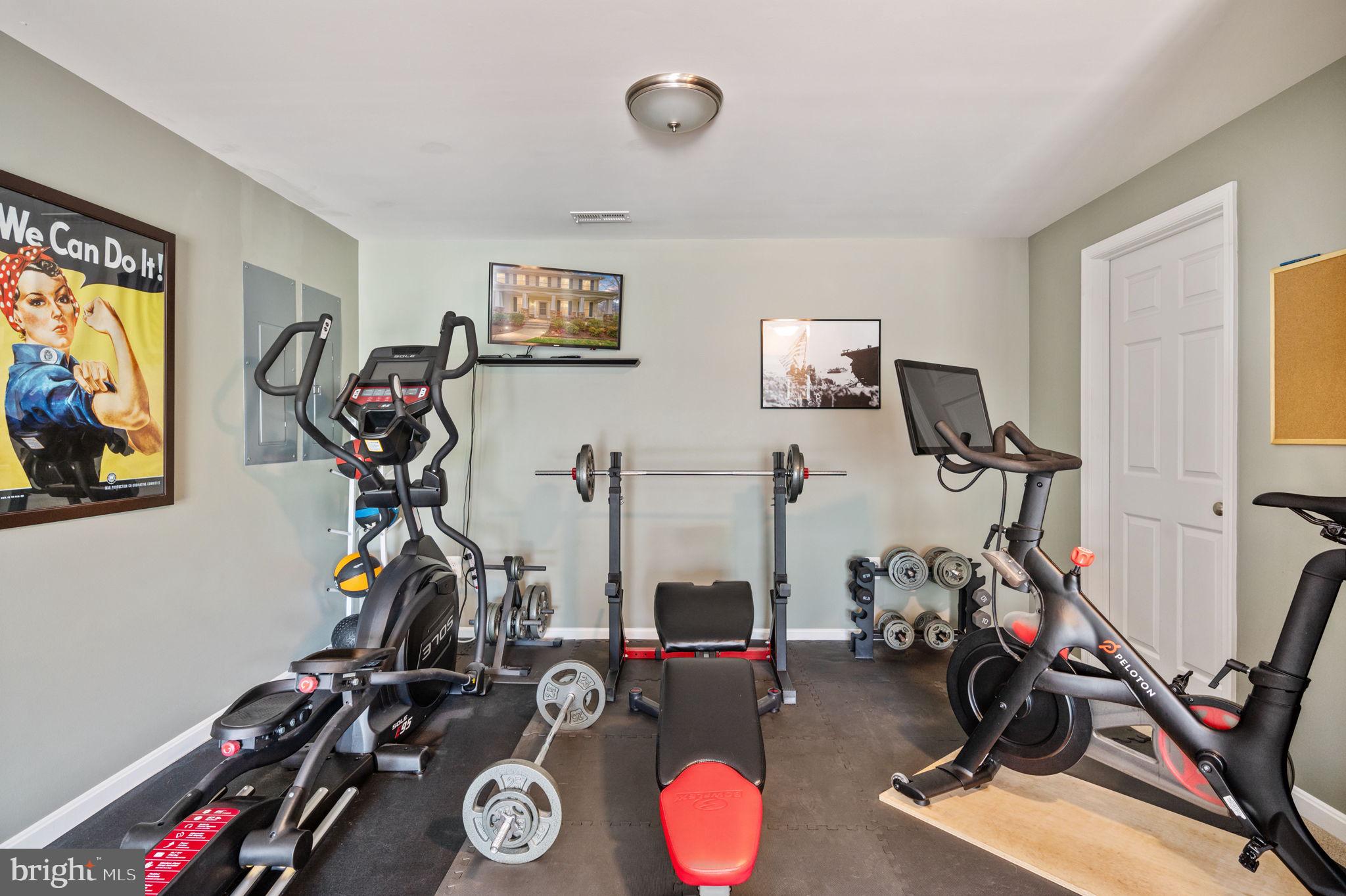 Home gym with exercise bikes, an elliptical, and a weight bench with barbells.