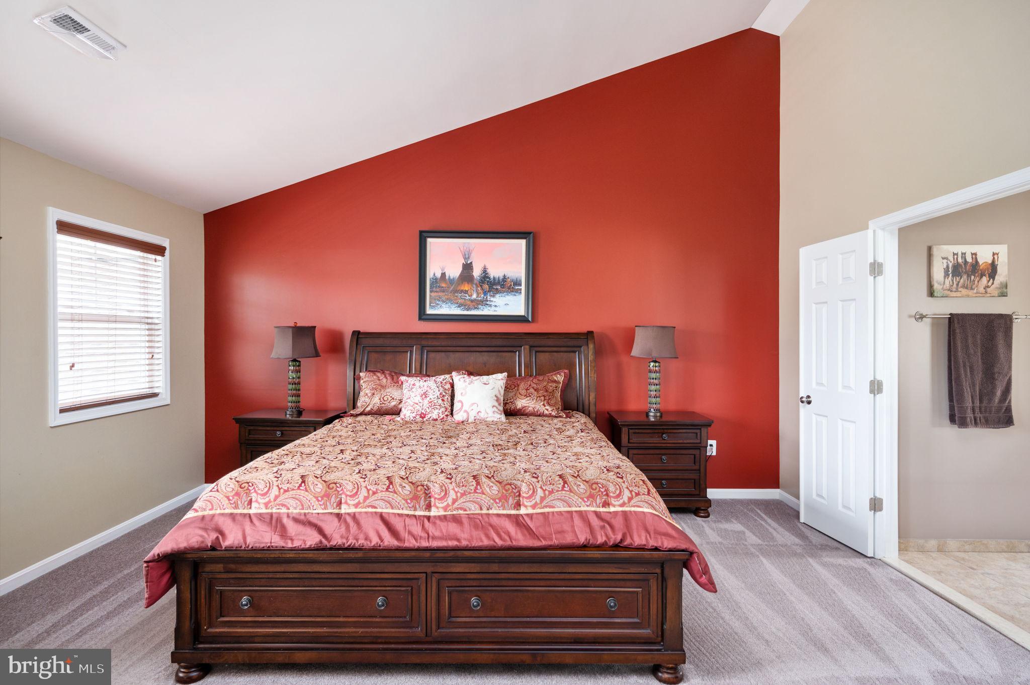 Furnished bedroom with patterned pink bedding, dark wood furniture, and a red accent wall.