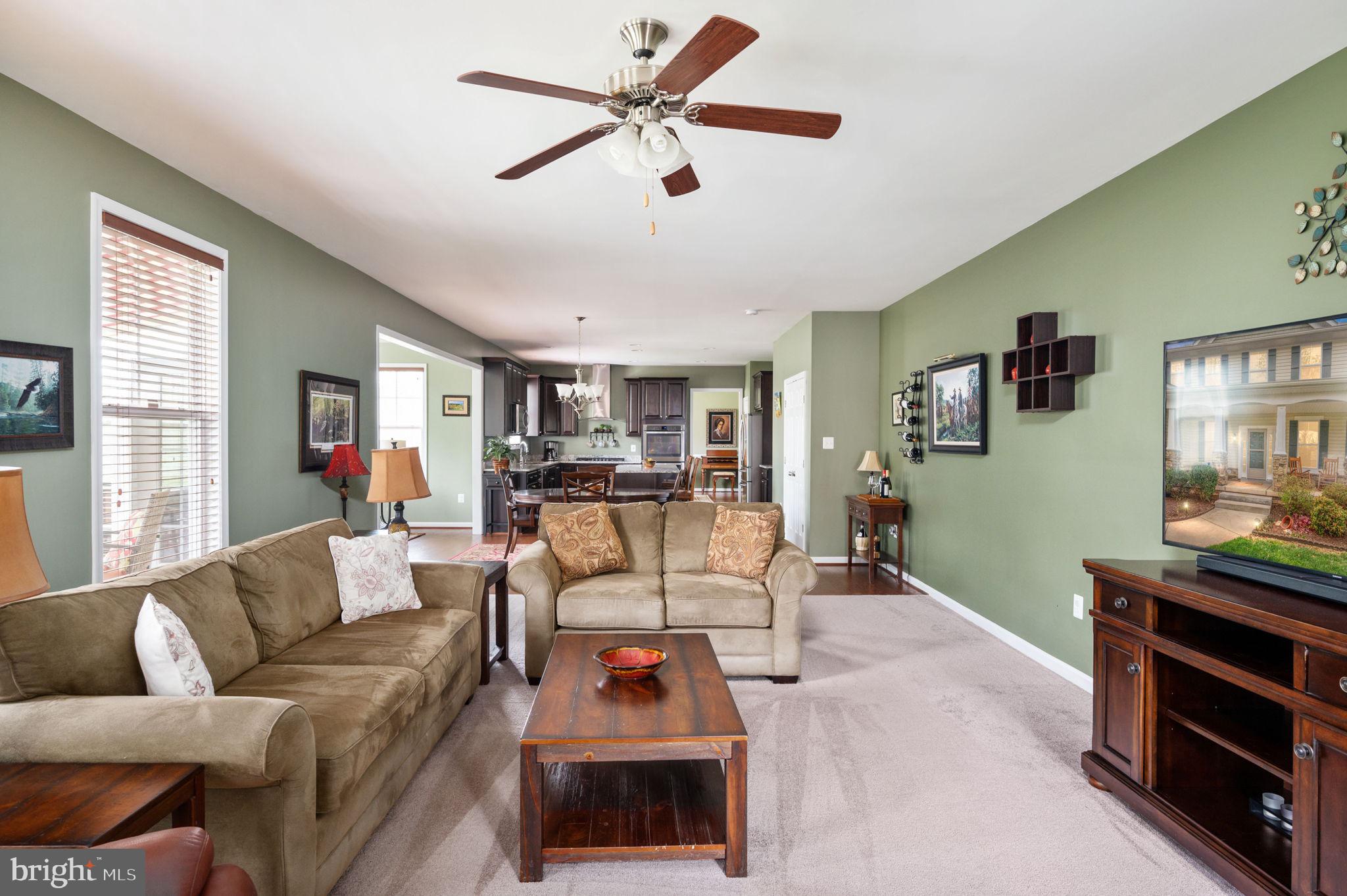 Furnished living room with sage-green walls and beige sofas, opening into the dining area and kitchen.