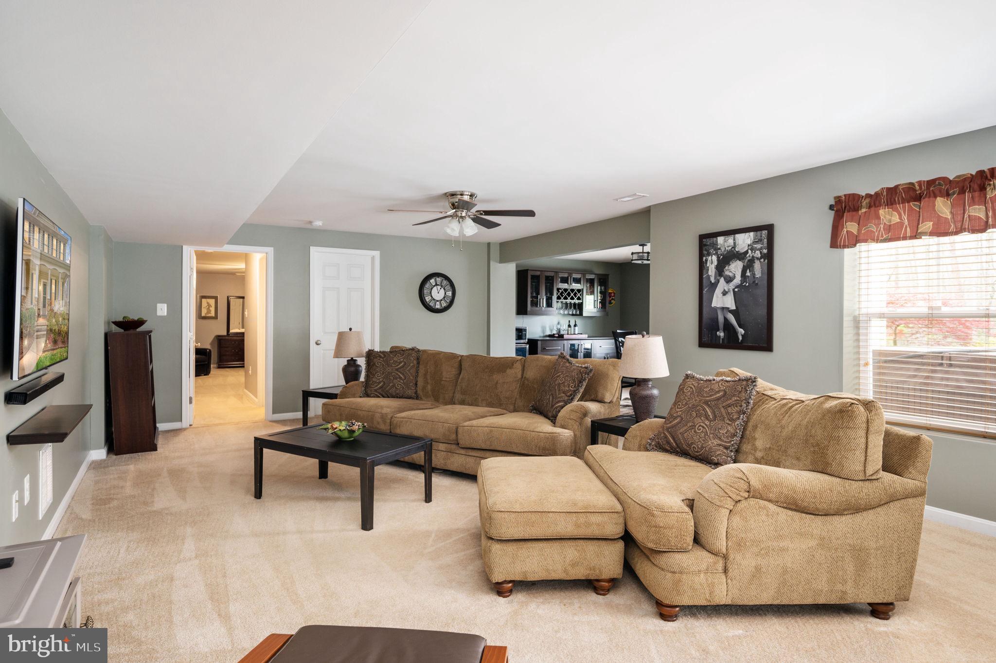 Furnished living room with tan sectional sofas, a dark coffee table, and an opening to the kitchen.