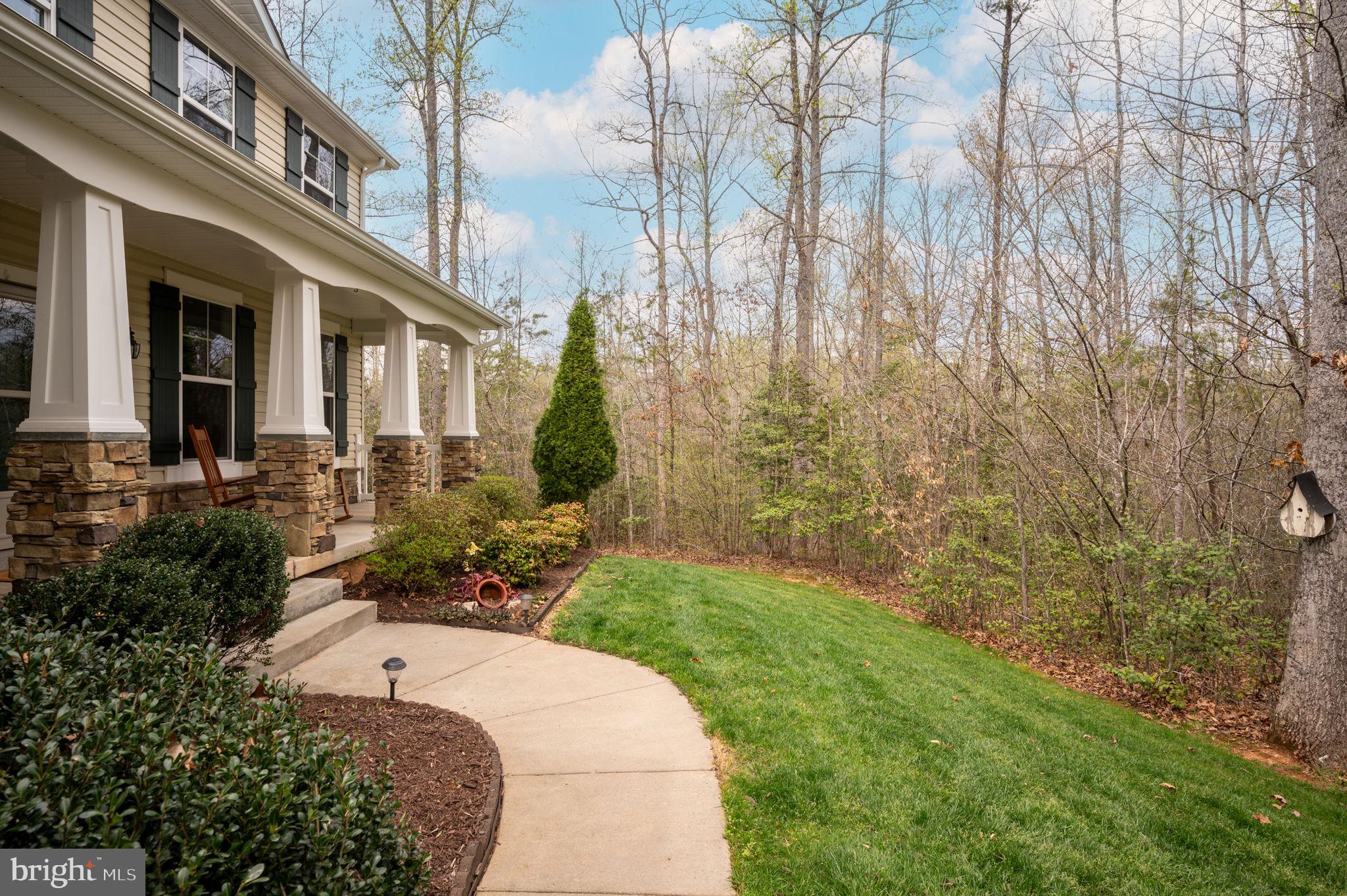 Home with a stone-columned porch beside a curved walkway and wooded backyard.