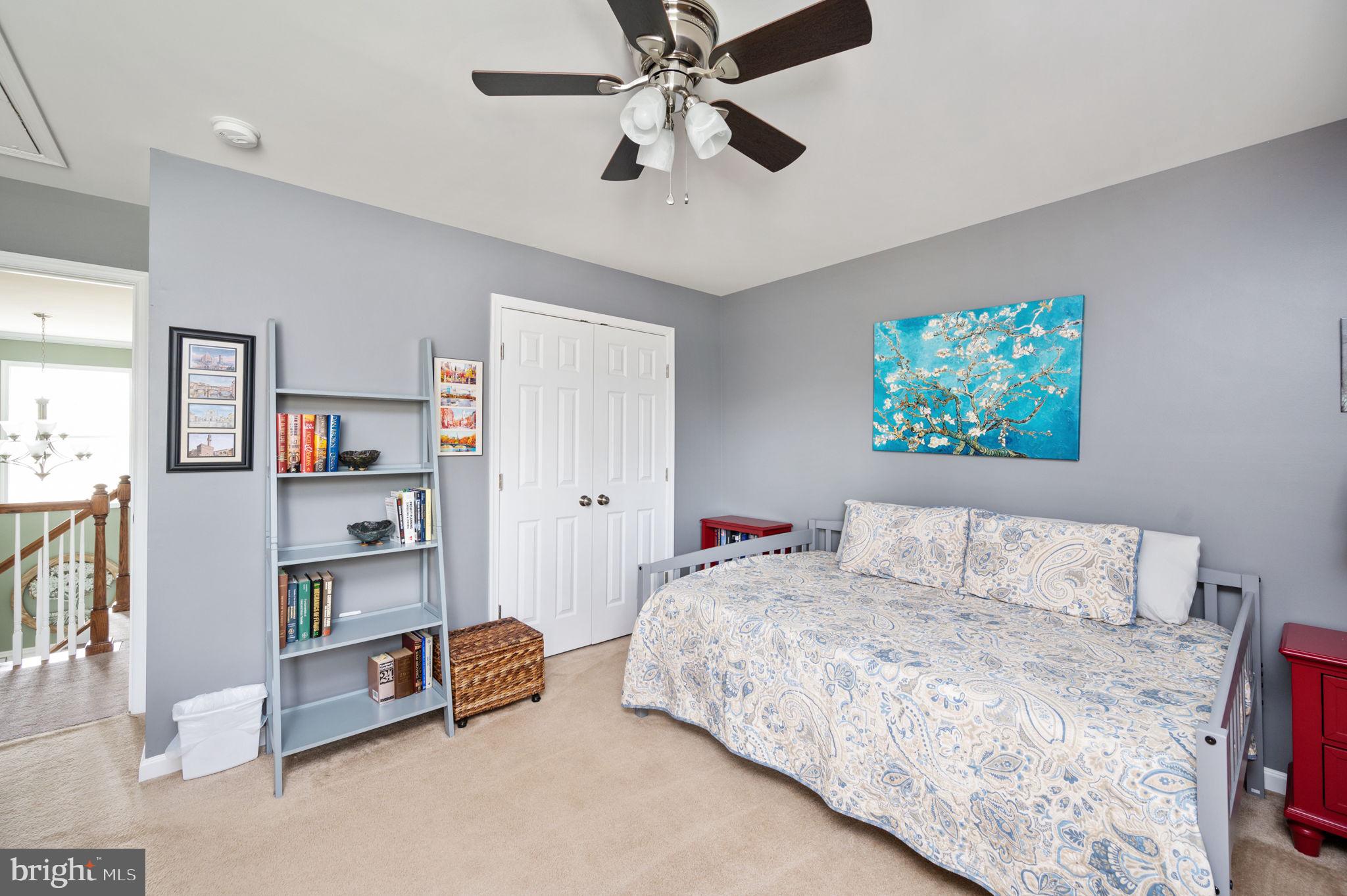 Bedroom with a patterned bed, gray walls, and a ceiling fan.