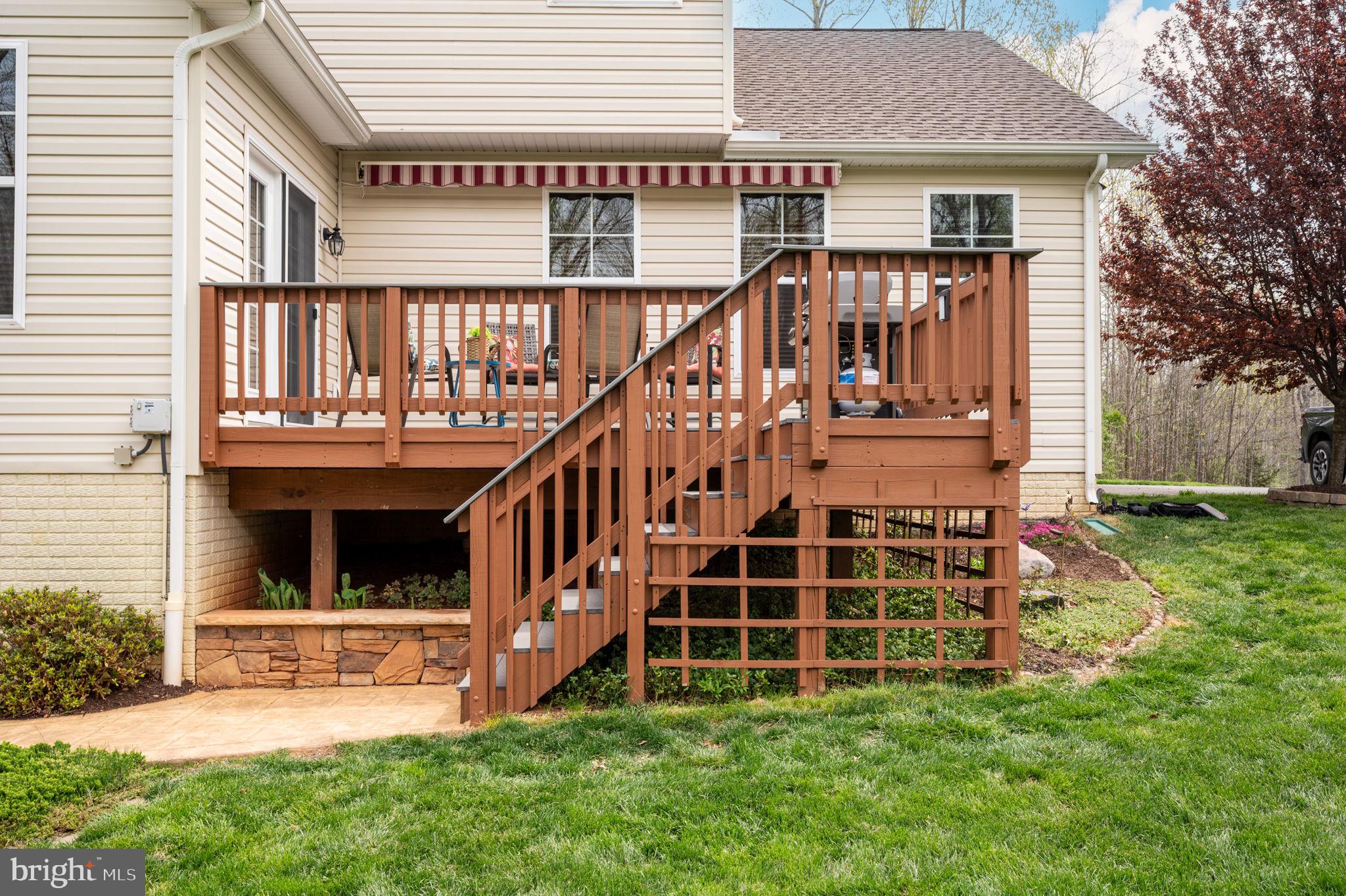 Raised wooden deck with stairs and railings behind a beige house, overlooking a green lawn.