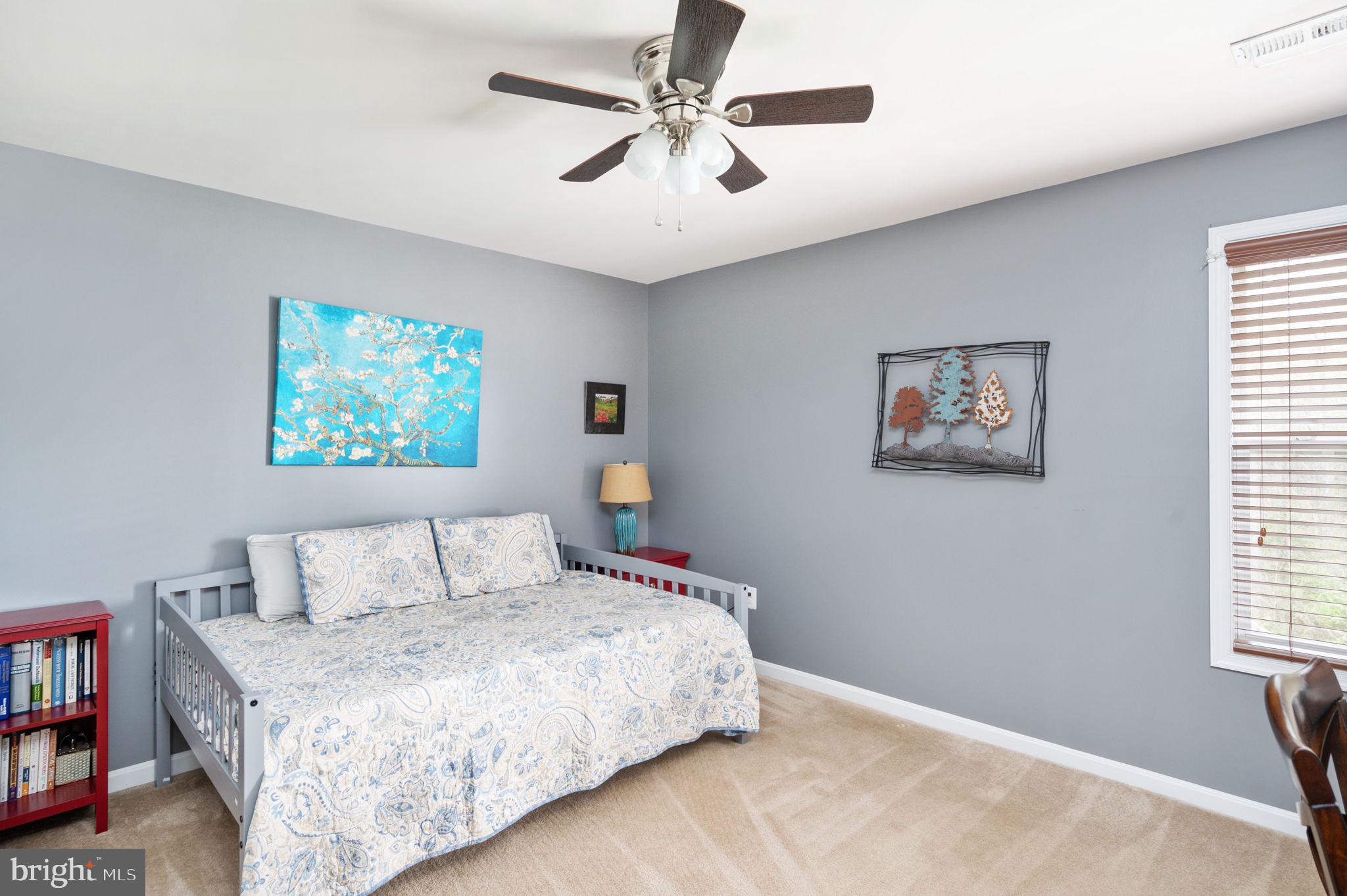 Furnished bedroom with a white daybed, blue-and-white bedding, gray walls, and a ceiling fan.