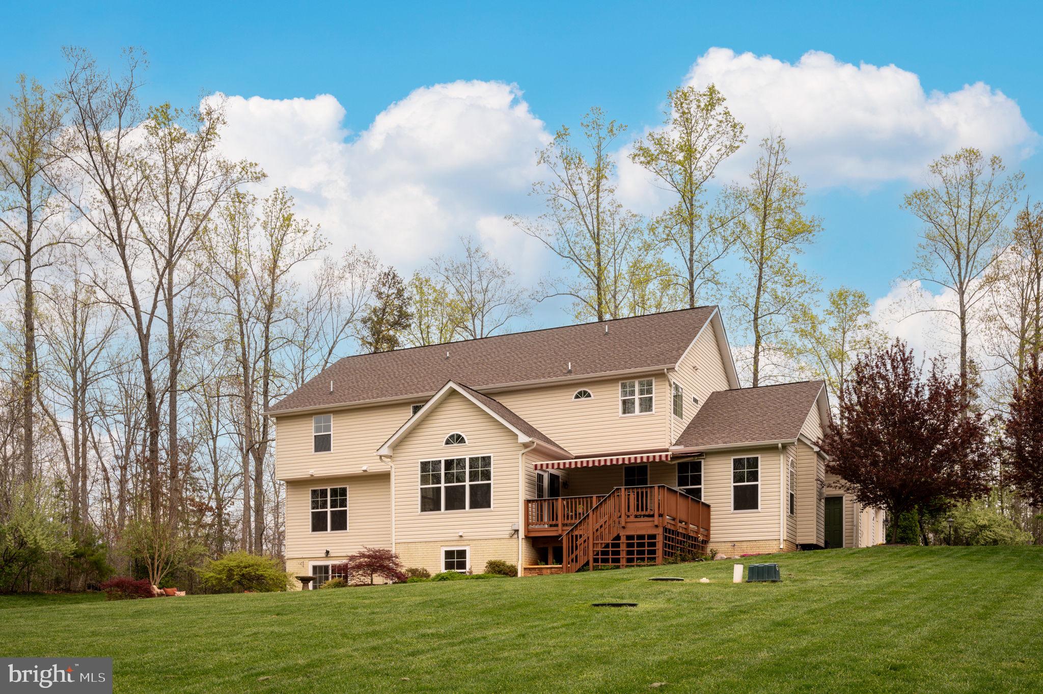 Rear of a beige two-story house with a raised deck and striped awning overlooking a broad lawn.