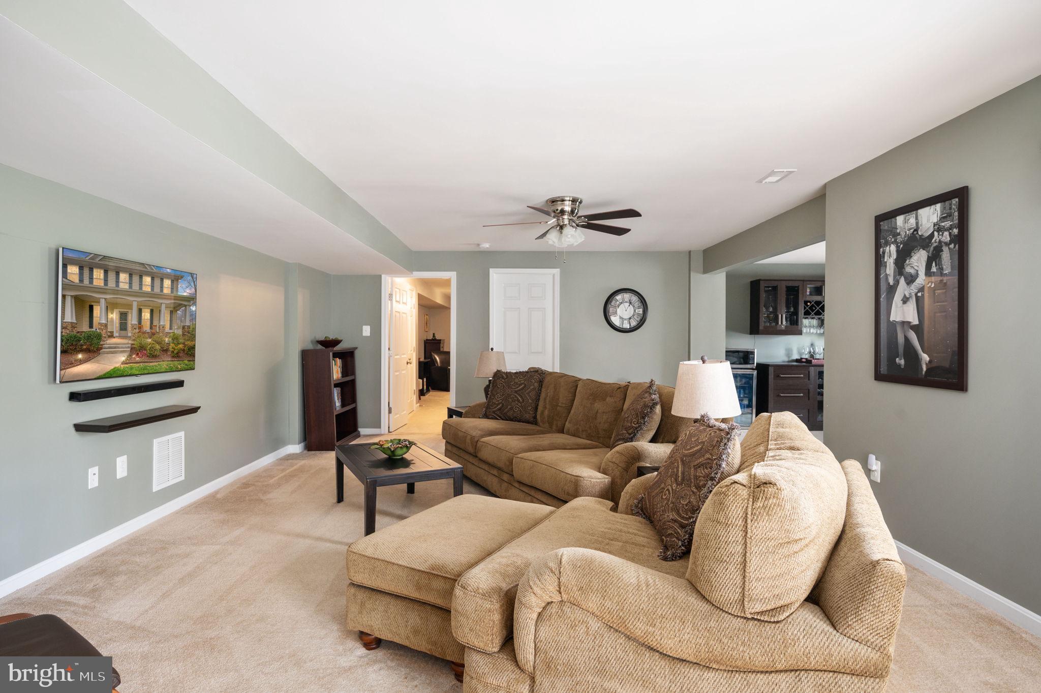 Furnished living room with tan sectional sofas, beige carpet, and an open view into the kitchen.