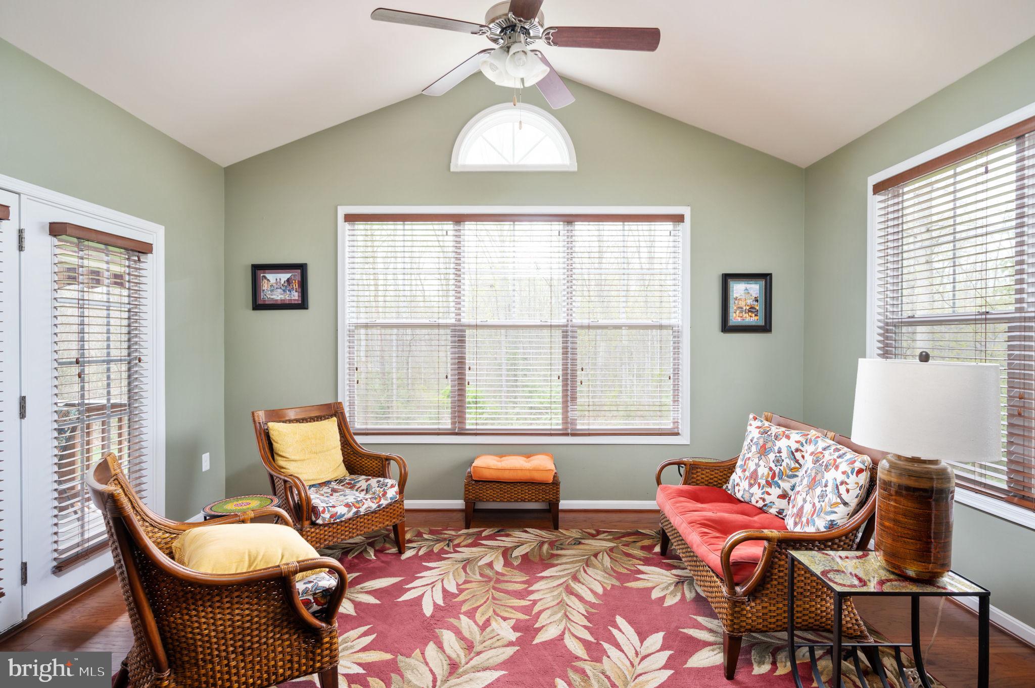 Furnished sunroom with wicker seating, a vaulted ceiling, and large windows with blinds.
