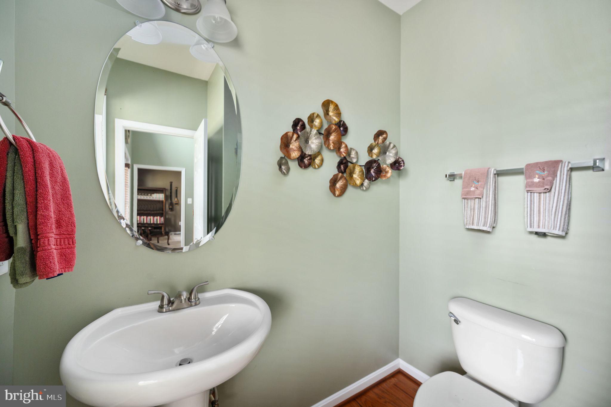 Bathroom with a pedestal sink, oval mirror, and decorative metal wall art.
