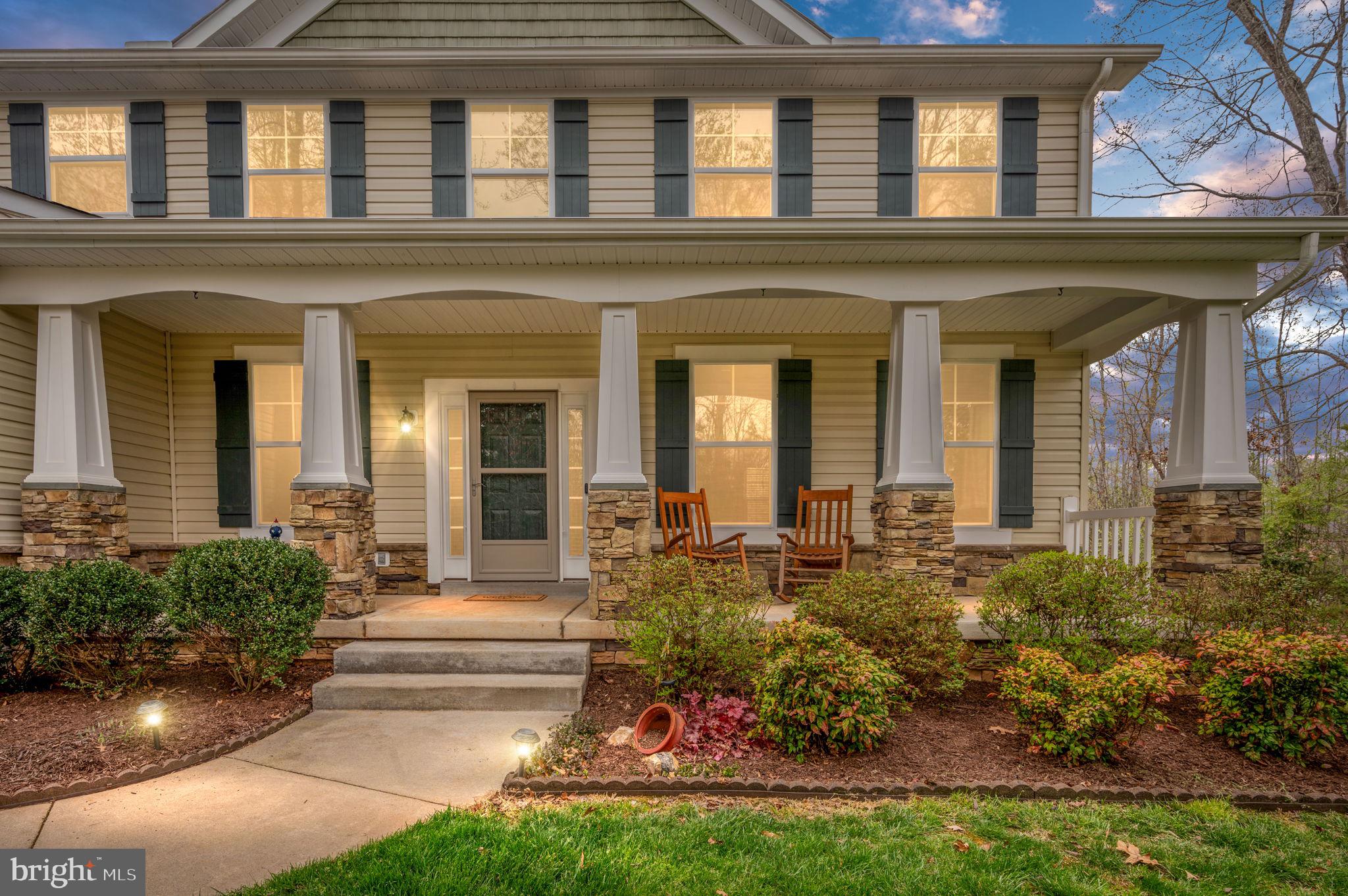 Two-story house with a deep covered porch, stone column bases, and wooden rocking chairs.