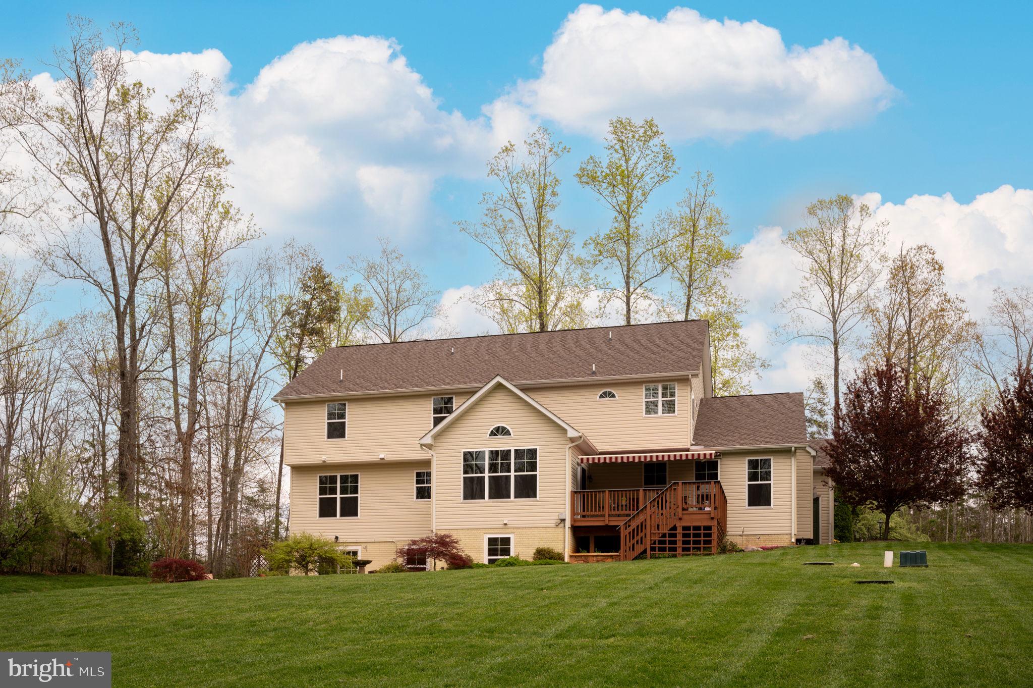 Rear of a two-story beige home with a raised deck, striped awning, and broad lawn.