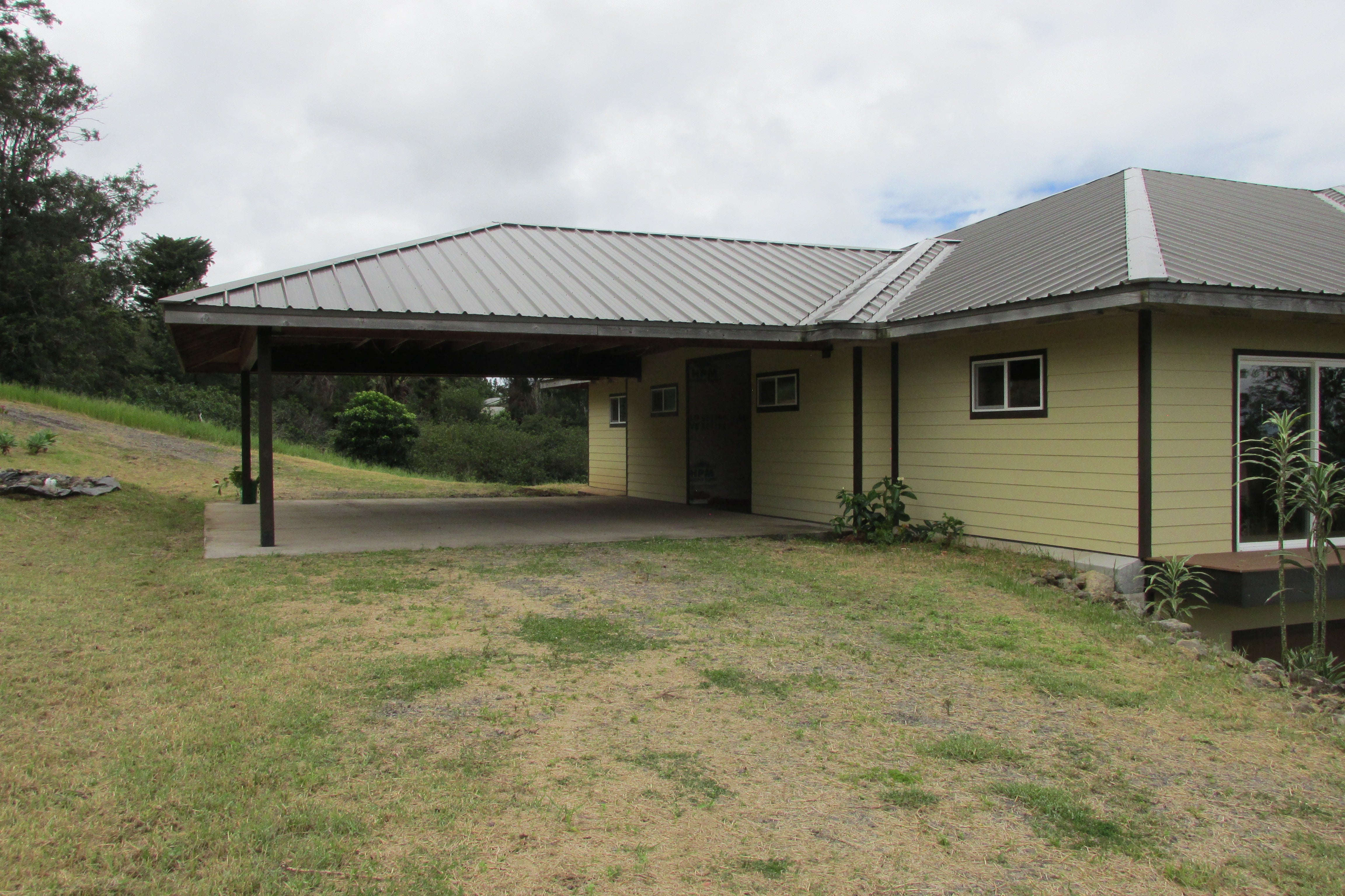 Single-story home with a metal roof and wide covered carport beside a sloping grassy yard.