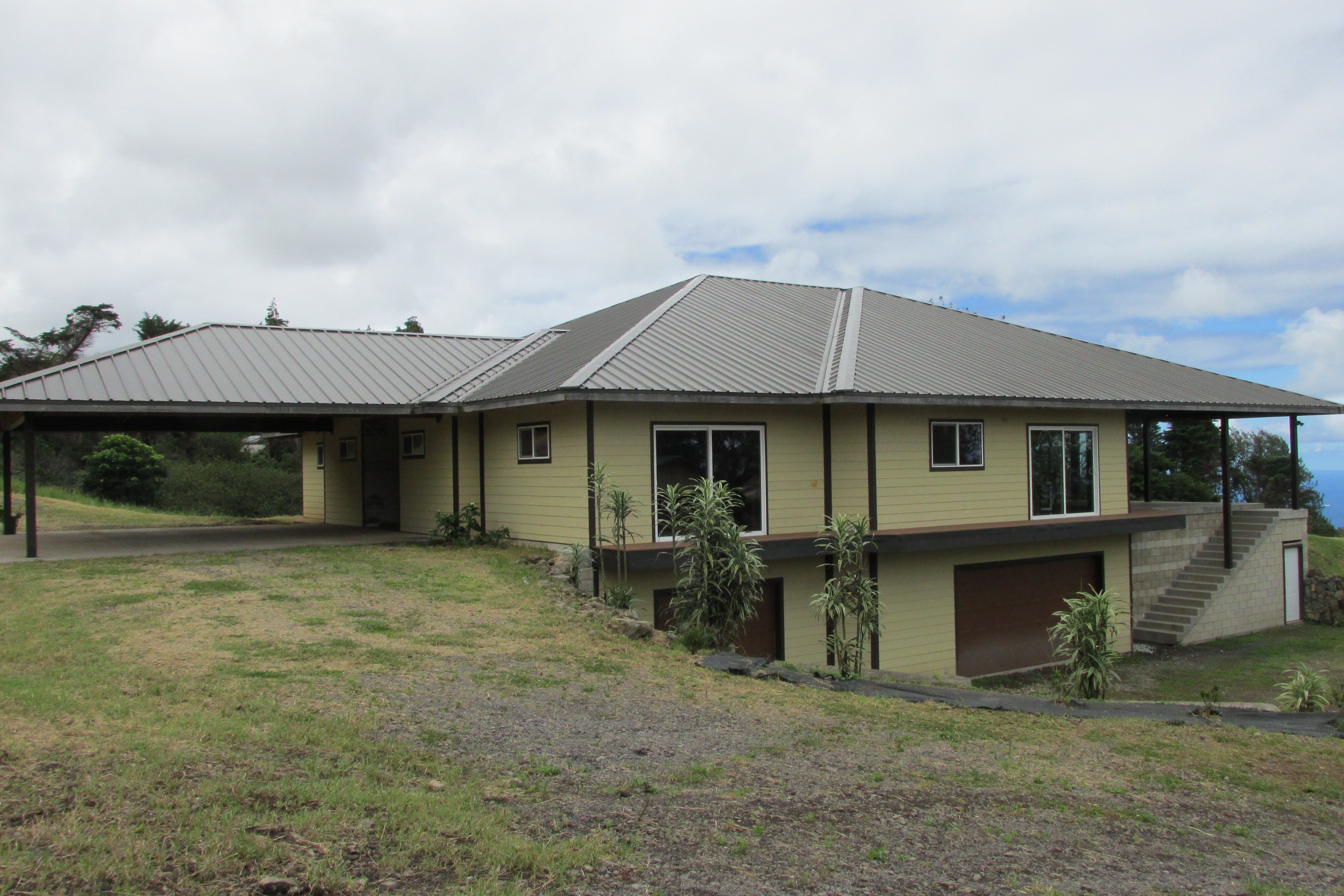 Home with a wide metal roof, covered carport, lower-level garage, and stairs on a grassy slope.