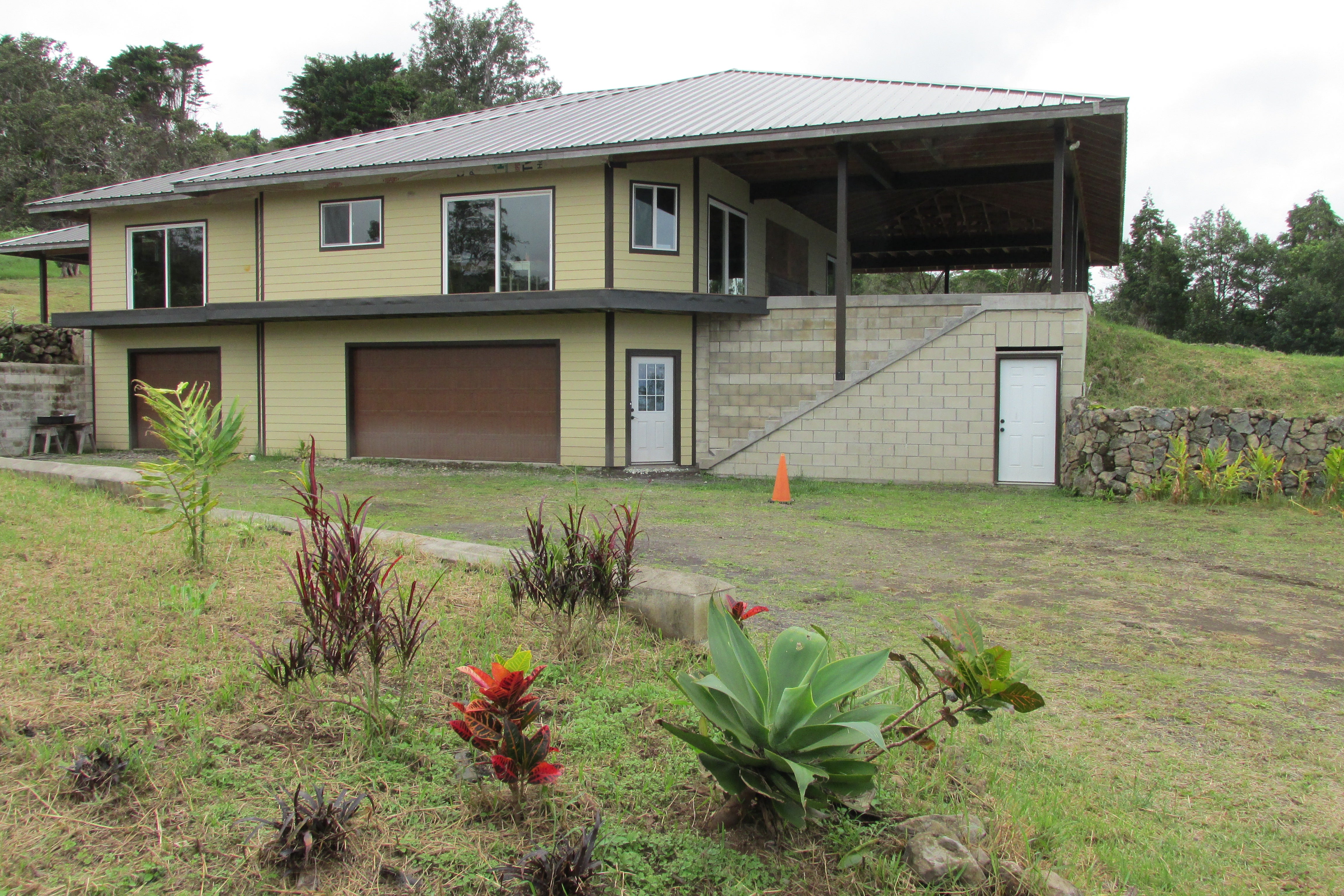 Pale yellow two-story home with a metal roof, covered lanai, and large garage.