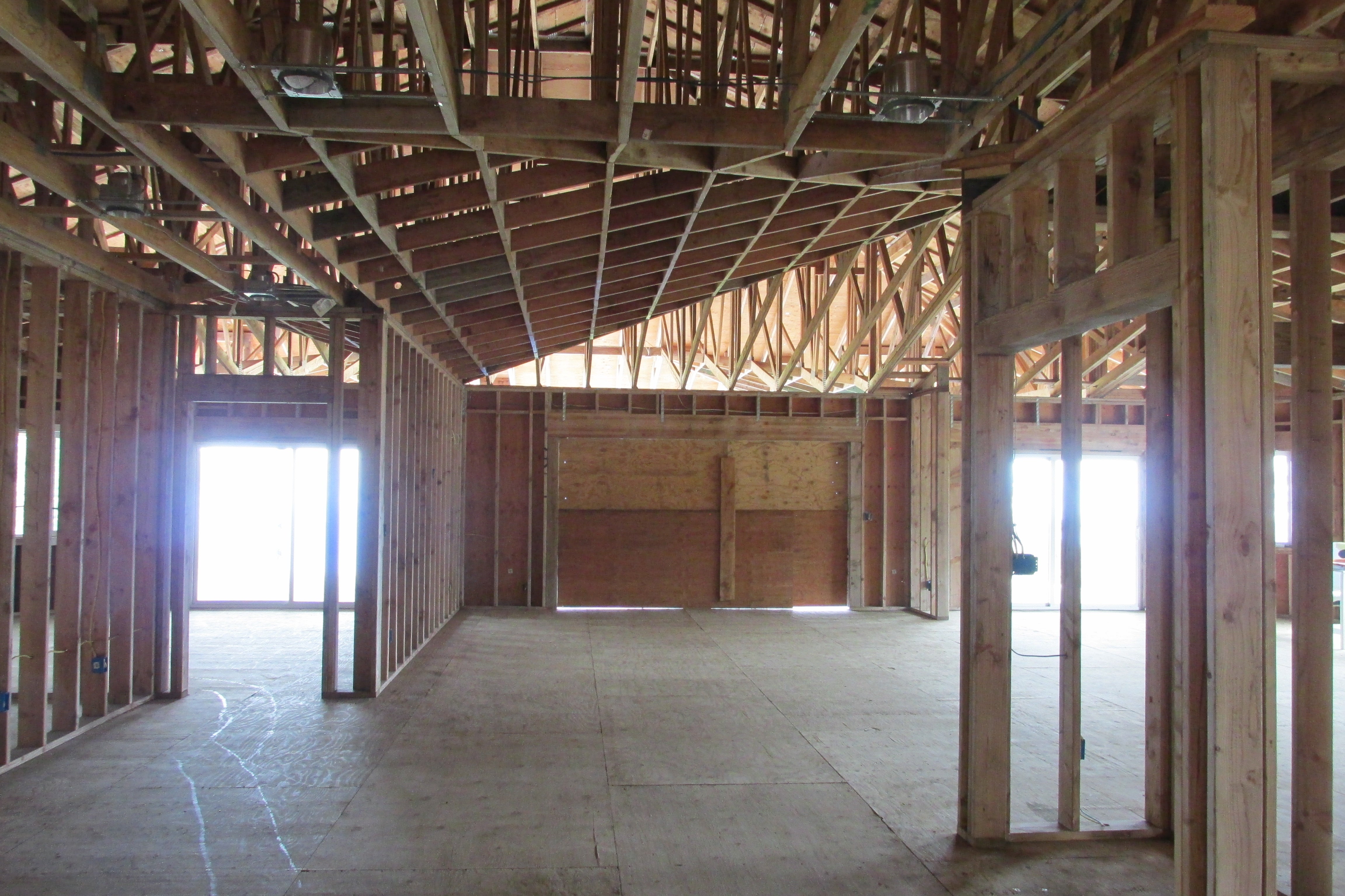 Unfinished home interior with exposed timber framing, open roof trusses, and large bright window openings.