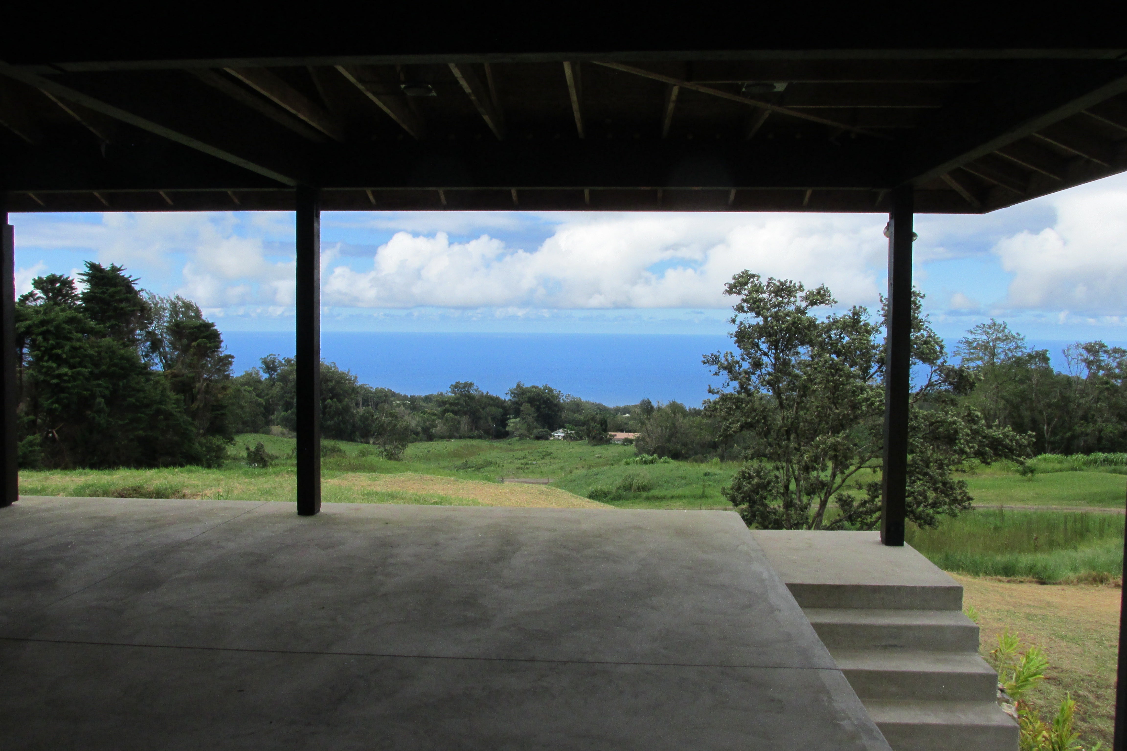Covered concrete patio overlooking green grounds and the ocean.
