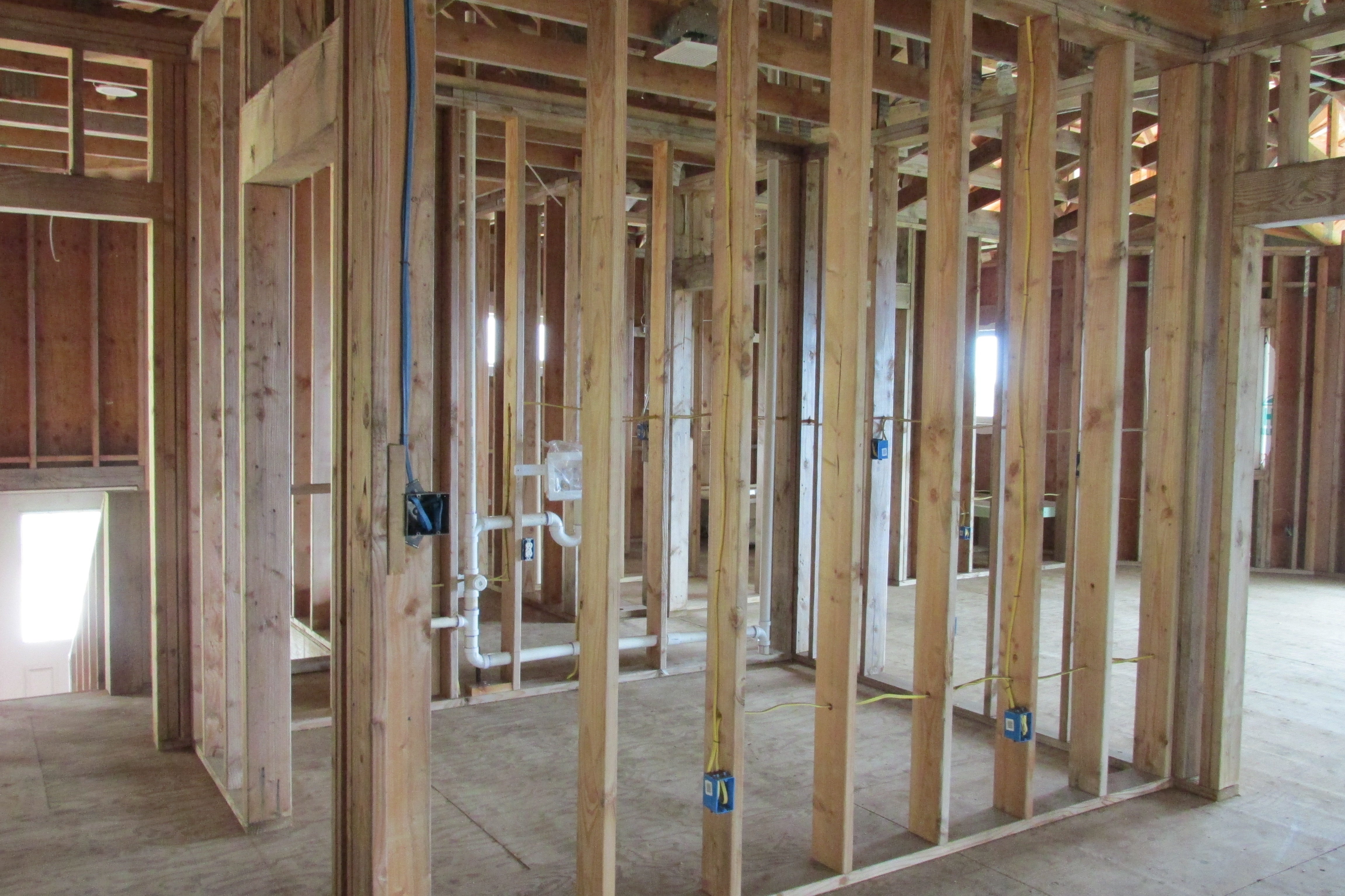 Unfinished house interior with exposed timber framing, plumbing pipes, and electrical wiring.