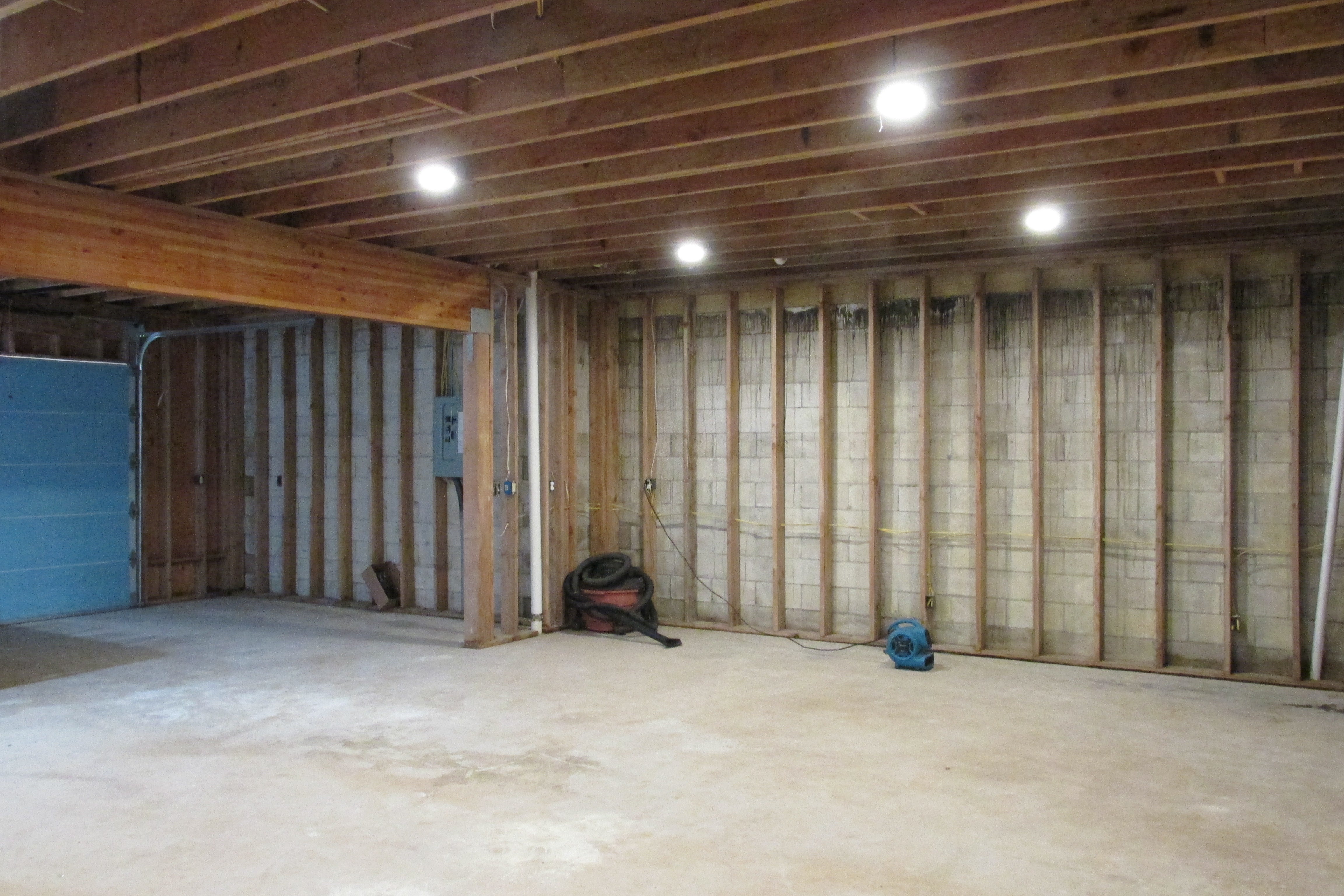 Unfinished garage with exposed framing, concrete floor, and blue garage door.