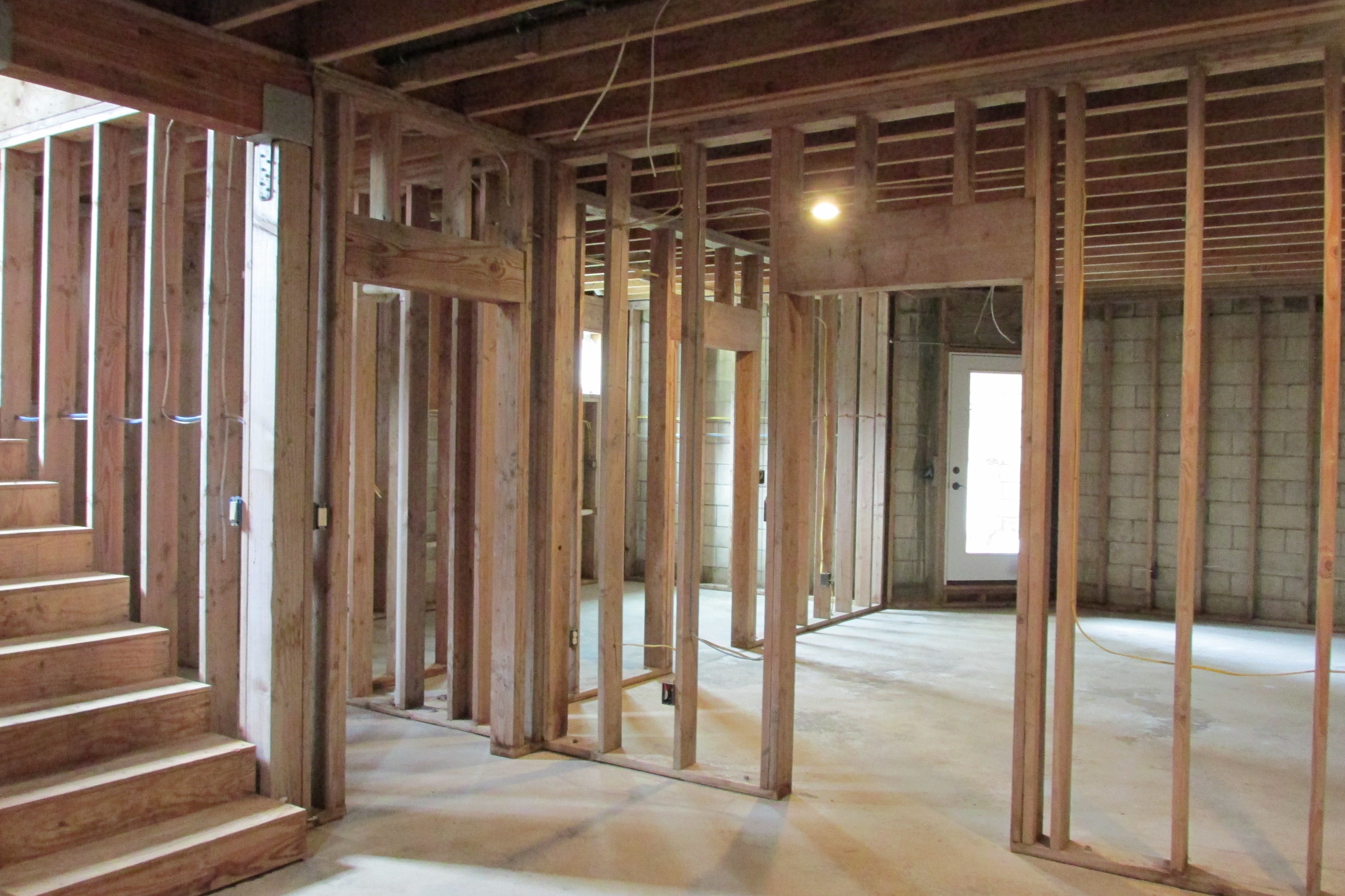Unfinished home interior with exposed framing, concrete floor, and a staircase.