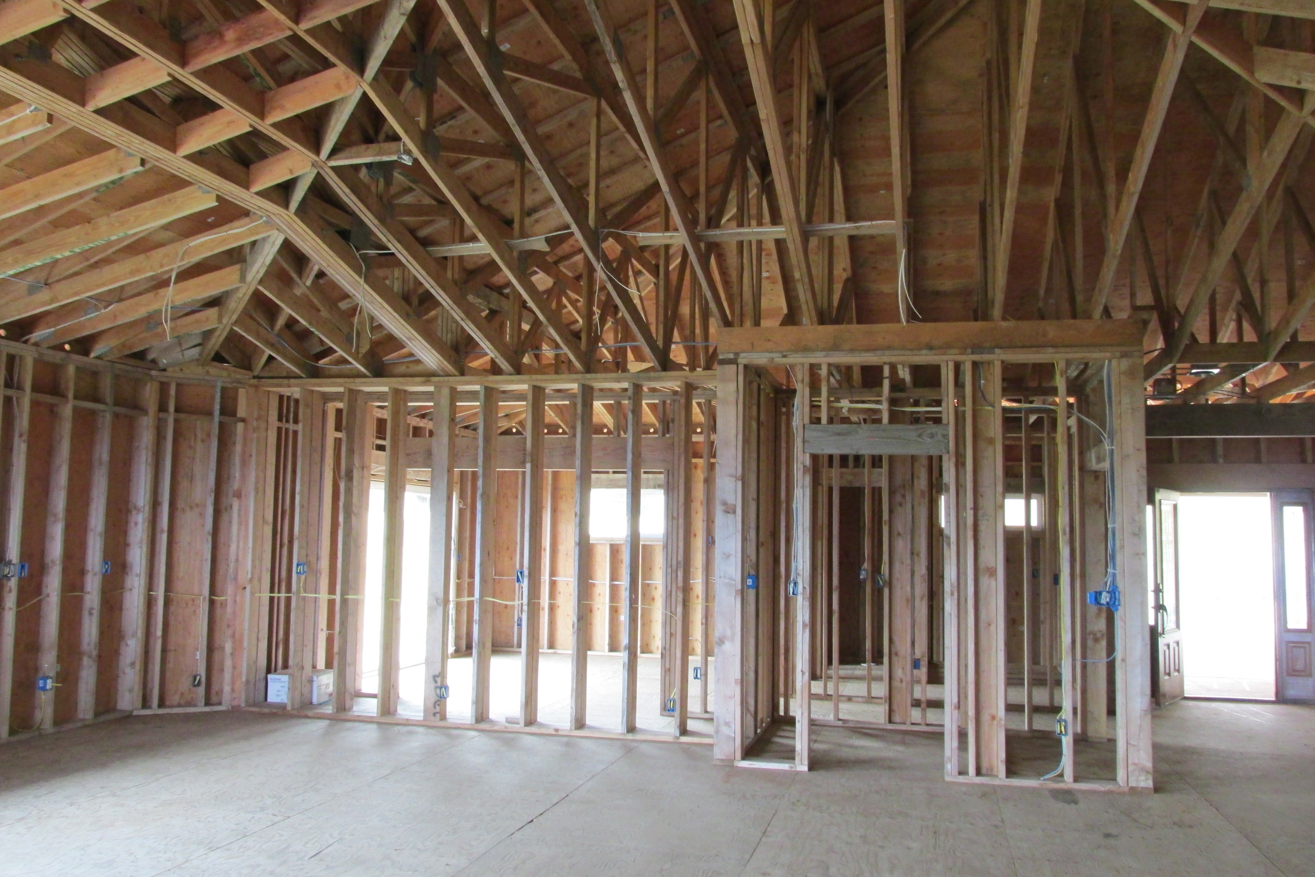 Unfinished house interior with exposed wood framing, roof trusses, and electrical wiring.