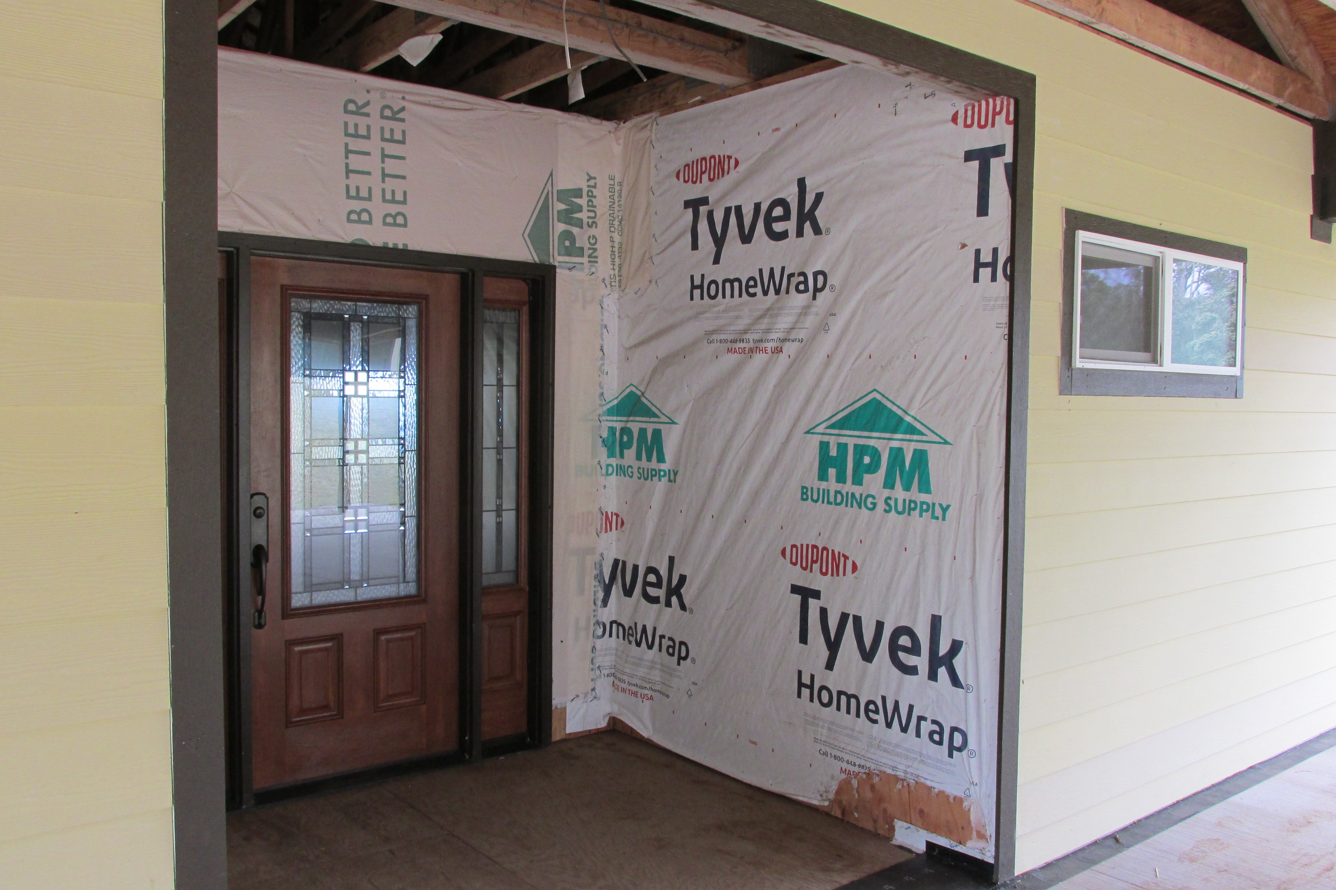 Home entry under construction with a decorative glass front door and exposed Tyvek wrap.
