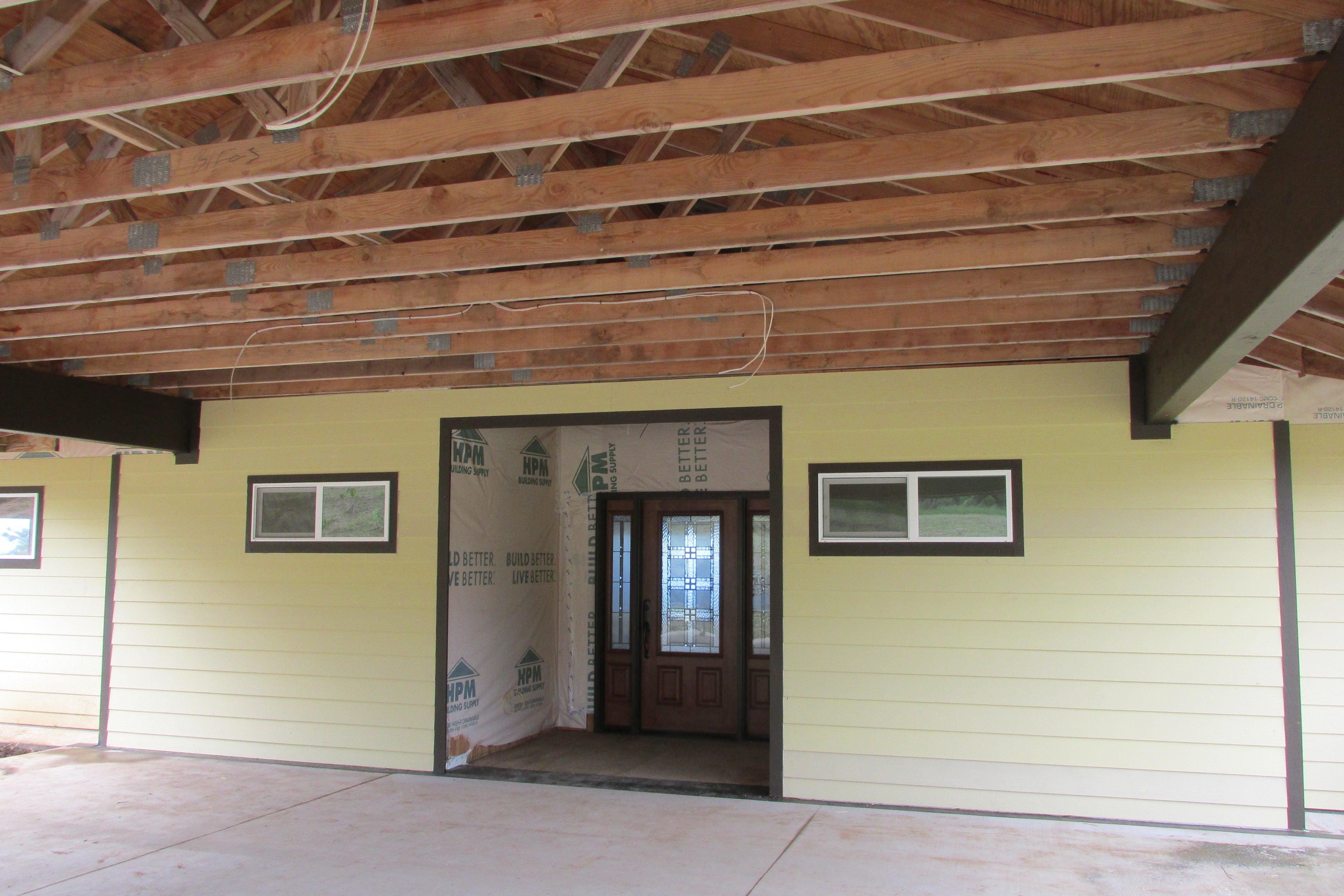 House entrance with a decorative-glass door beneath an unfinished exposed-wood porch roof.