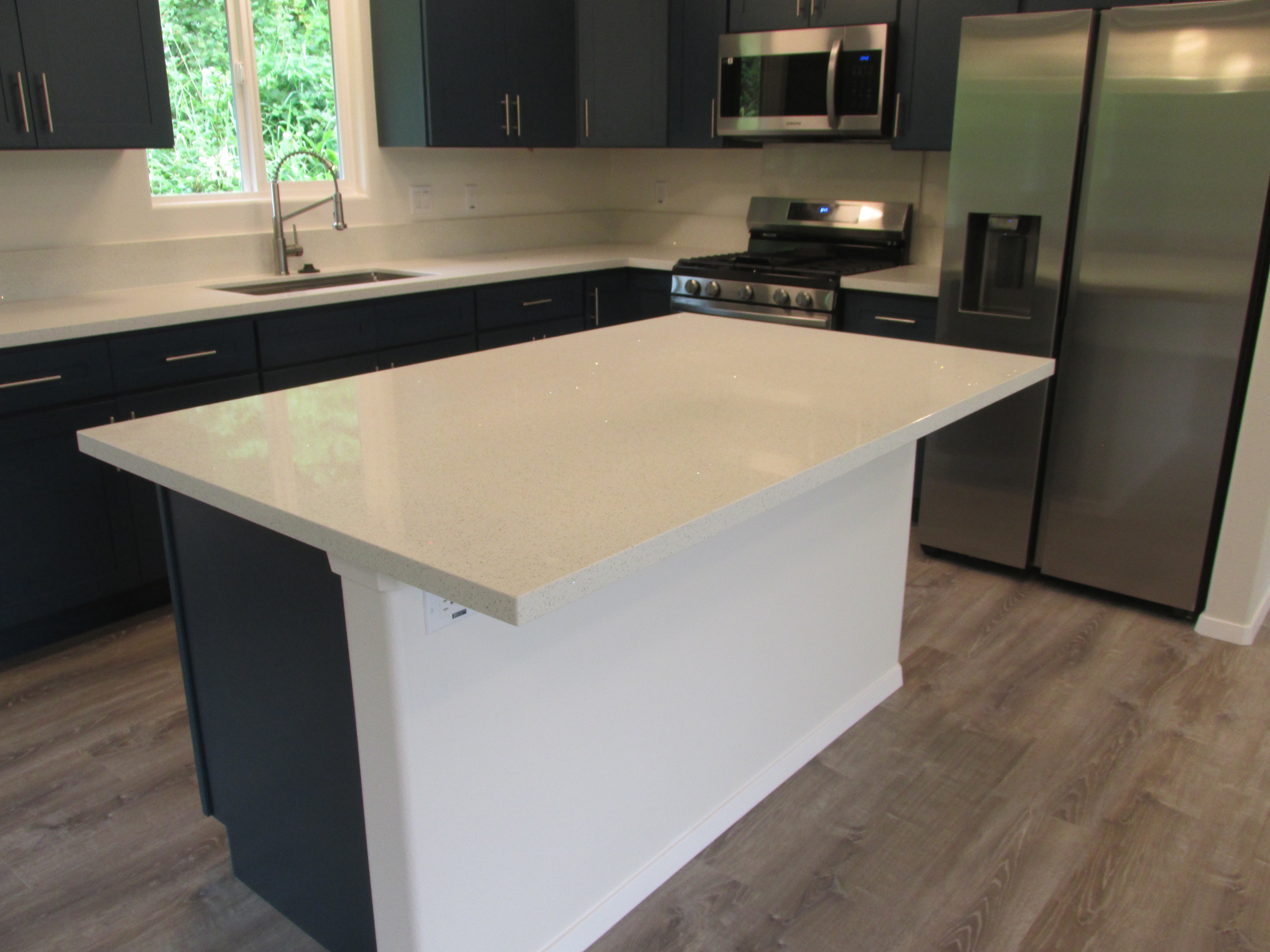 Modern kitchen with a large white island, dark cabinets, and stainless steel appliances.