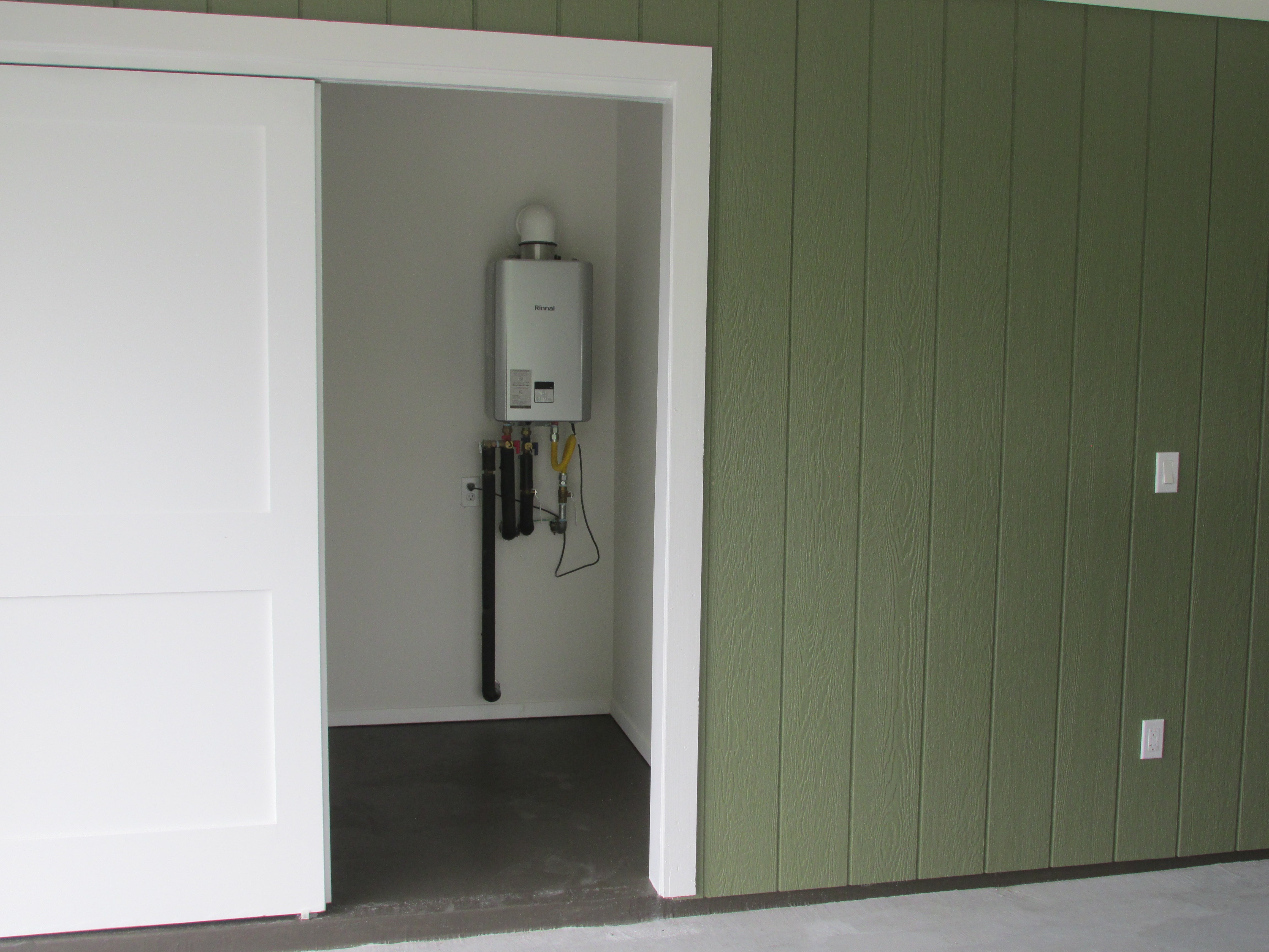 Tankless water heater in an open utility closet beside green siding and a white sliding door.