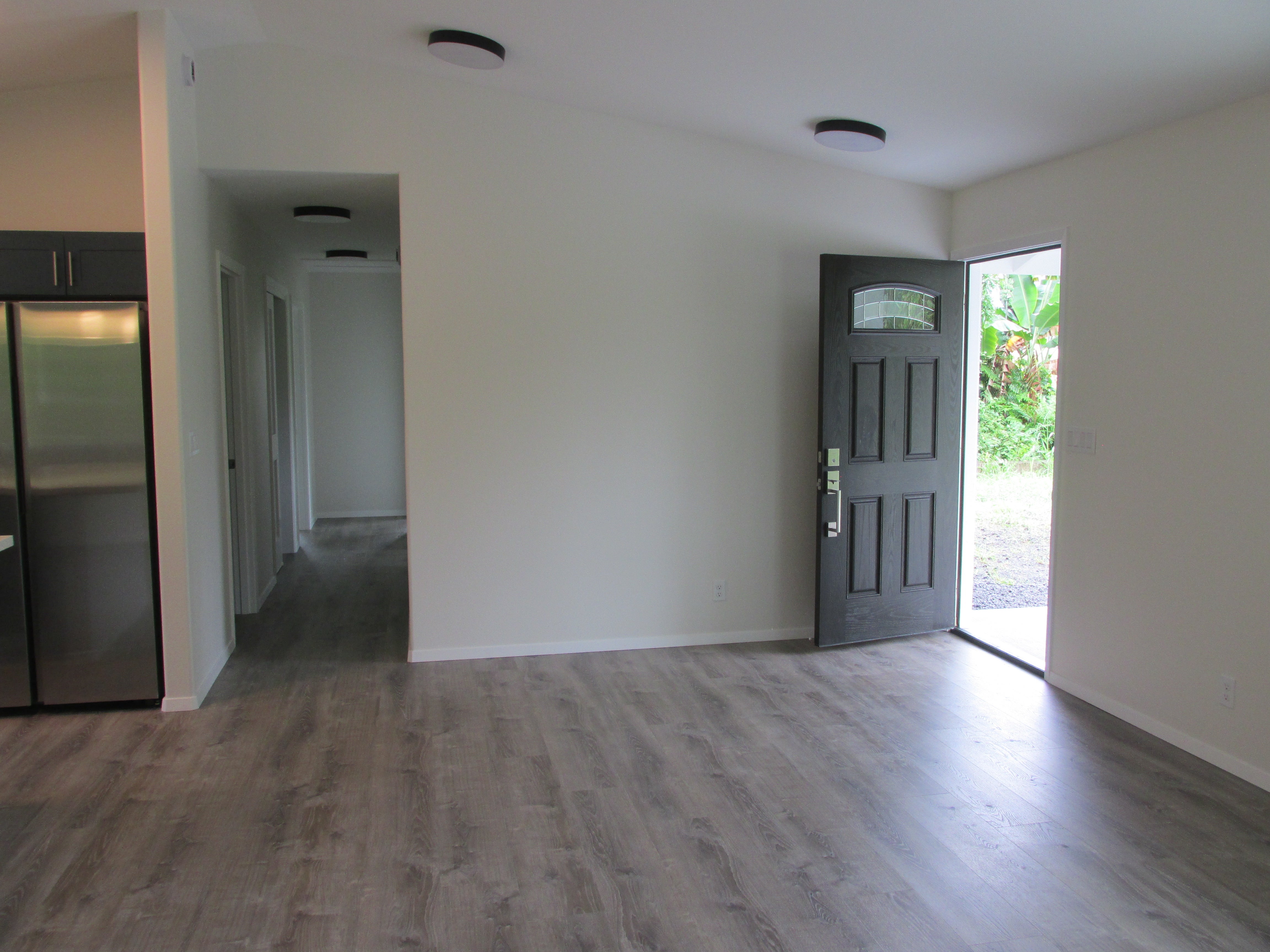 Open living area with gray flooring, a dark front door, and a hallway beside the kitchen.
