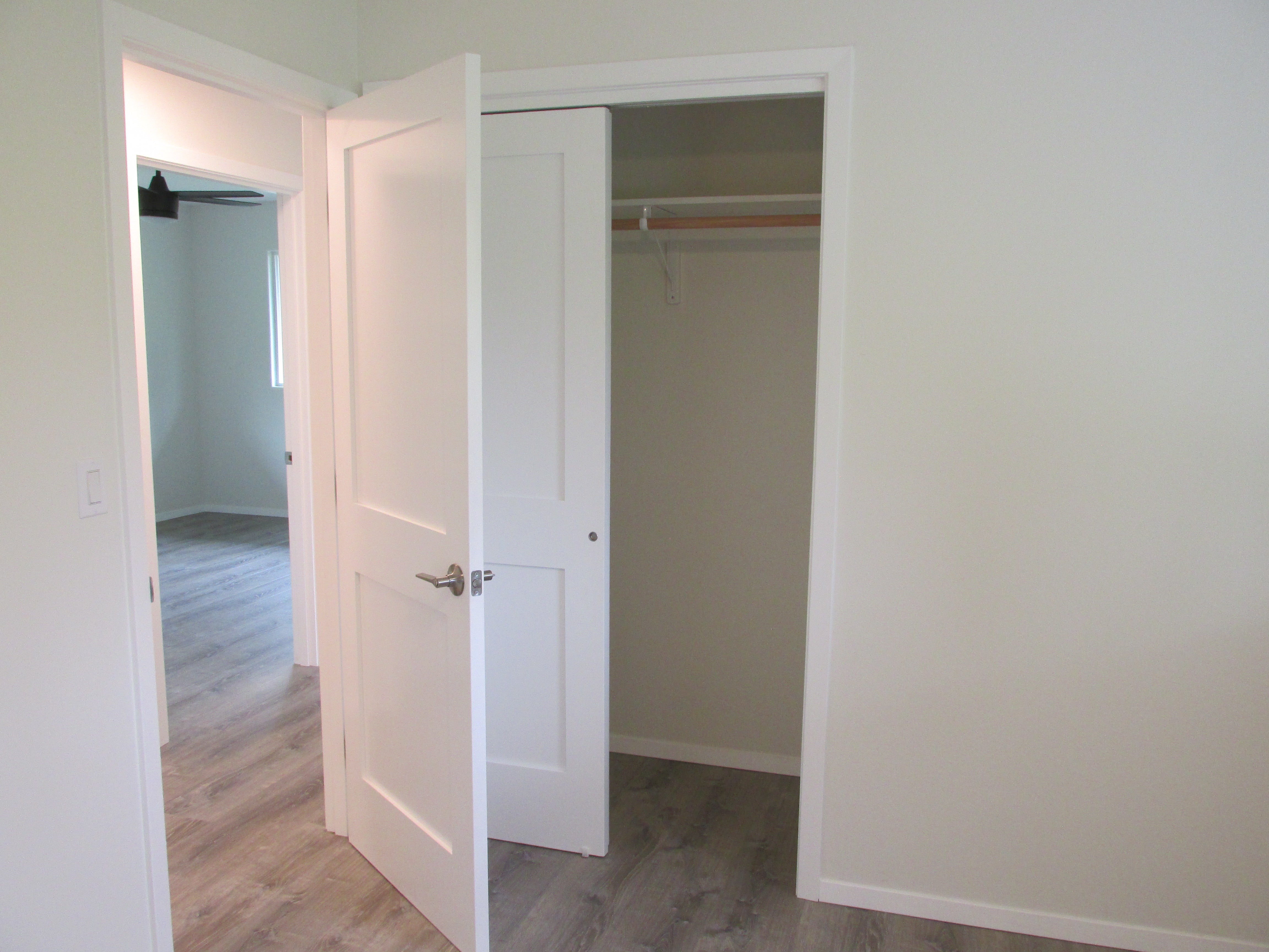 Empty bedroom closet with open white doors, a hanging rod, and gray wood-look flooring.