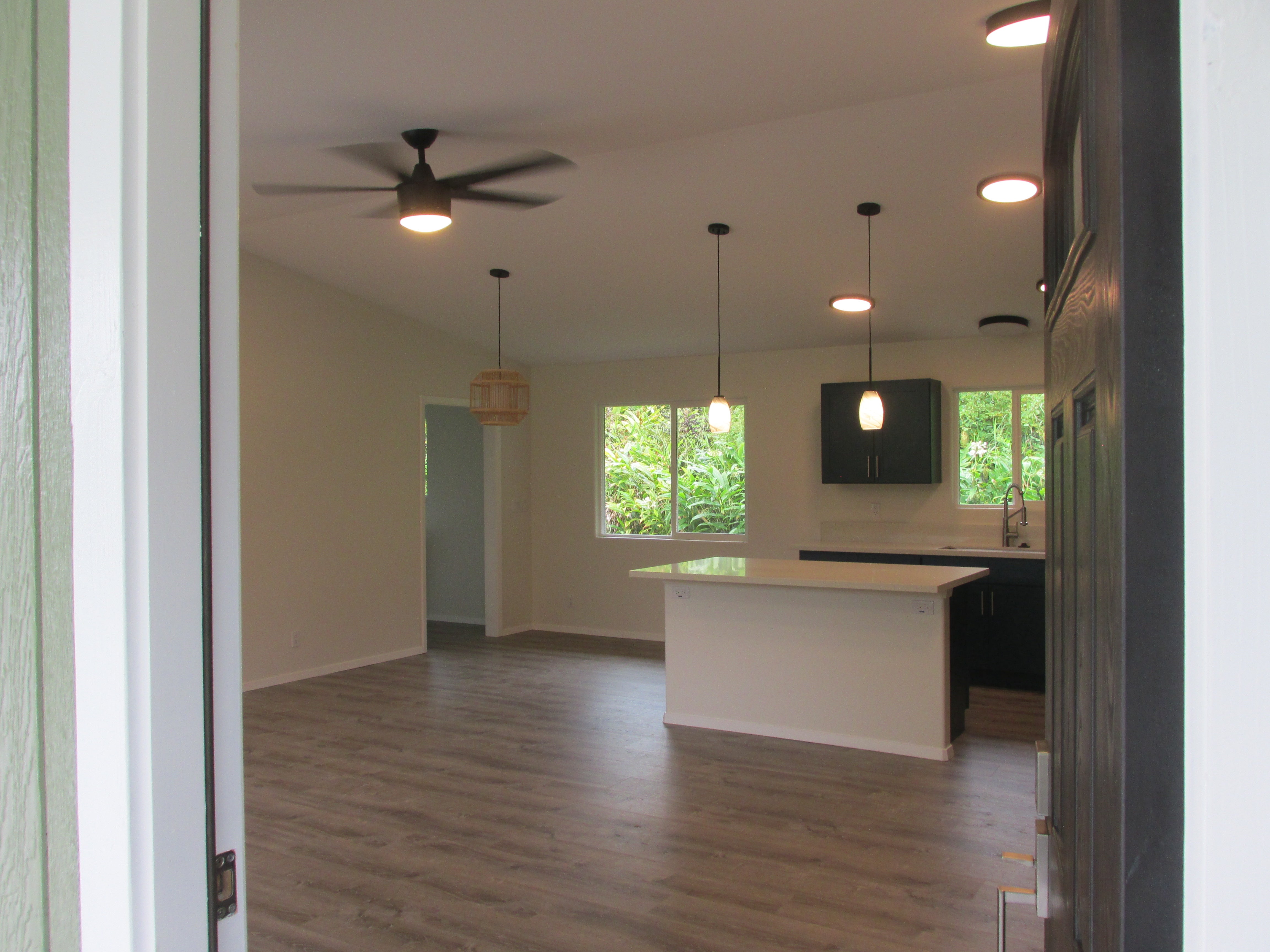 Open-plan kitchen with dark cabinets, a white island, and windows overlooking lush greenery.