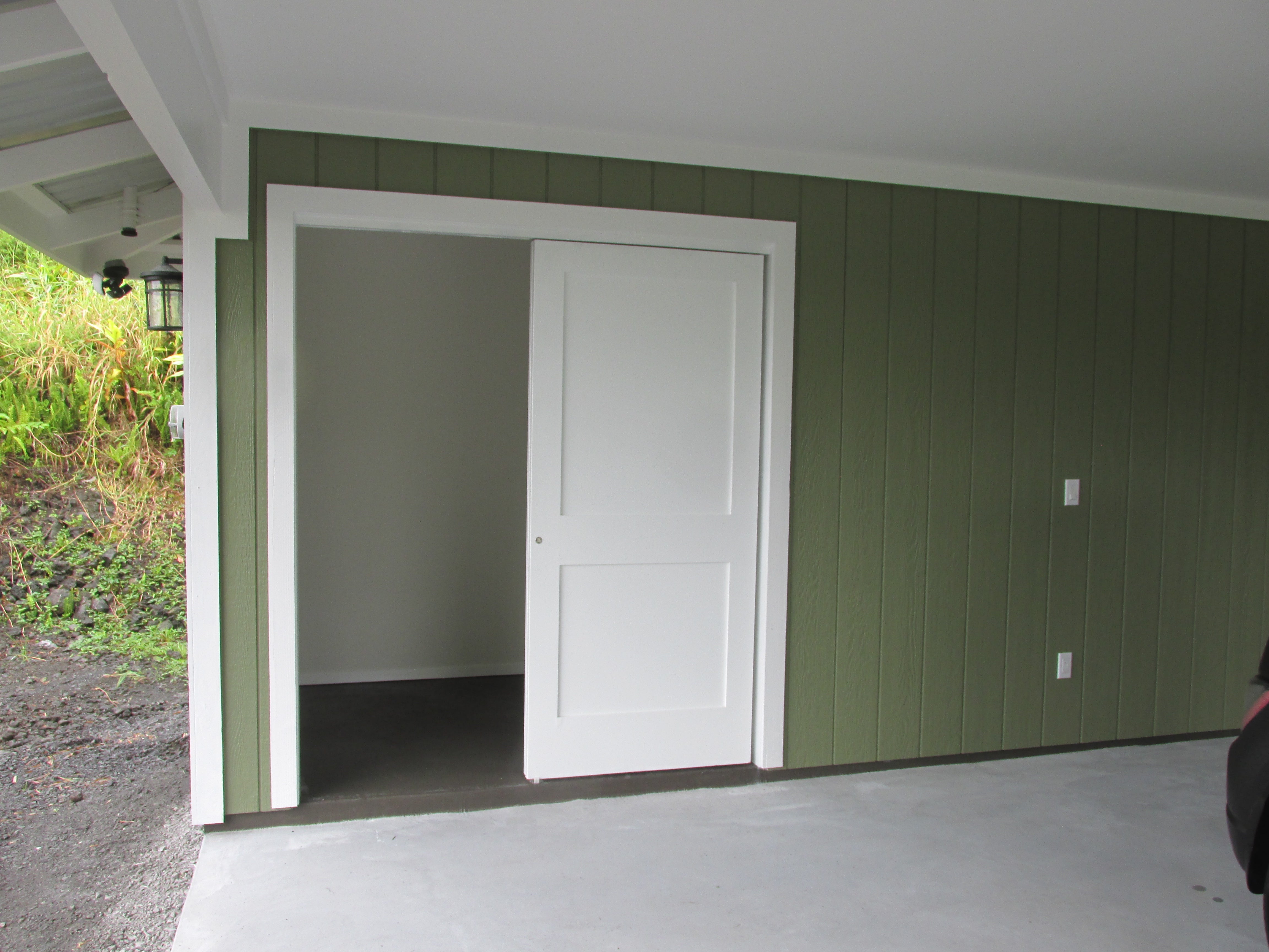 Covered entry with green siding and an open white door leading into an empty room.