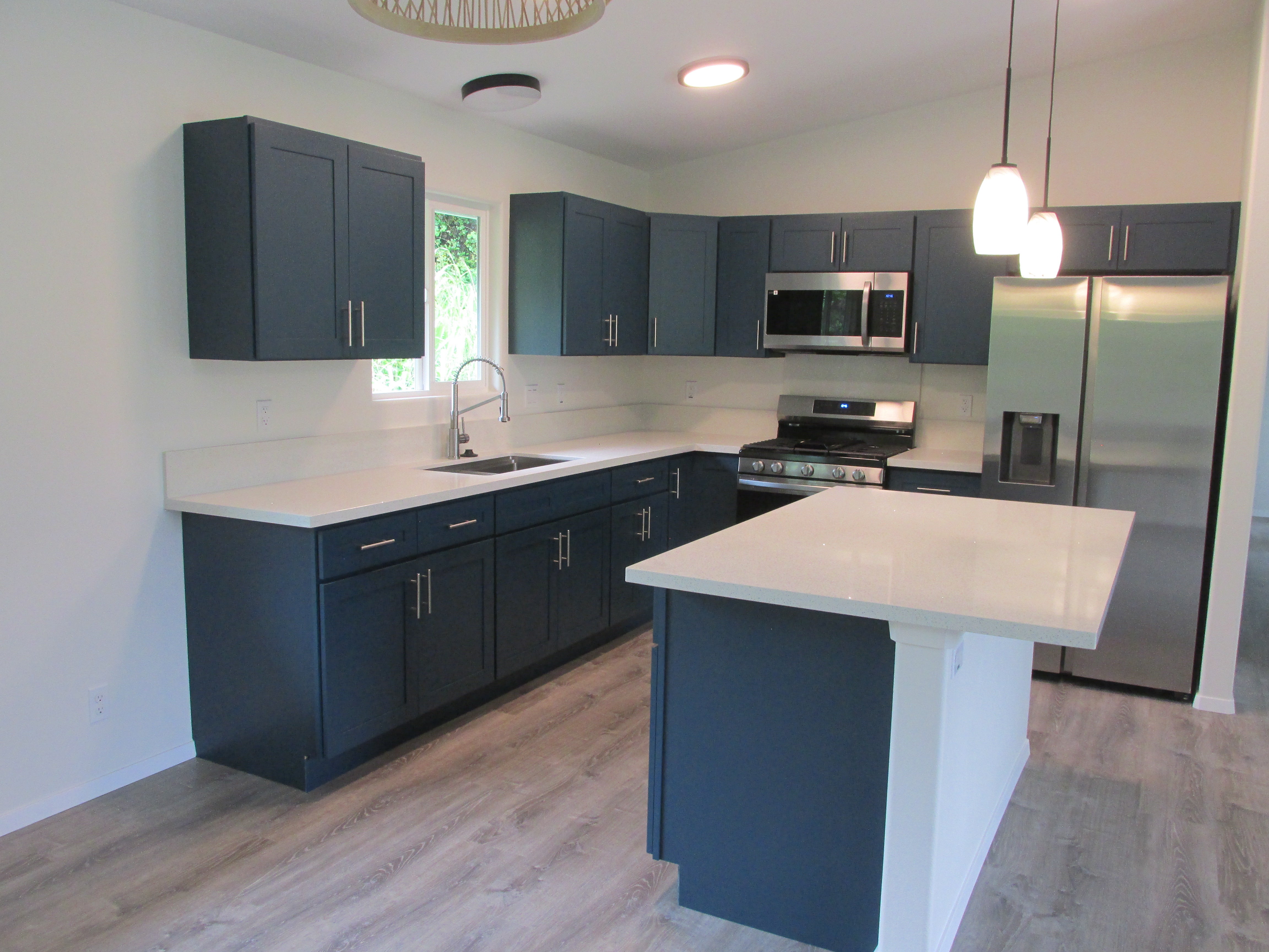 Modern kitchen with dark blue cabinets, white island, and stainless steel appliances.