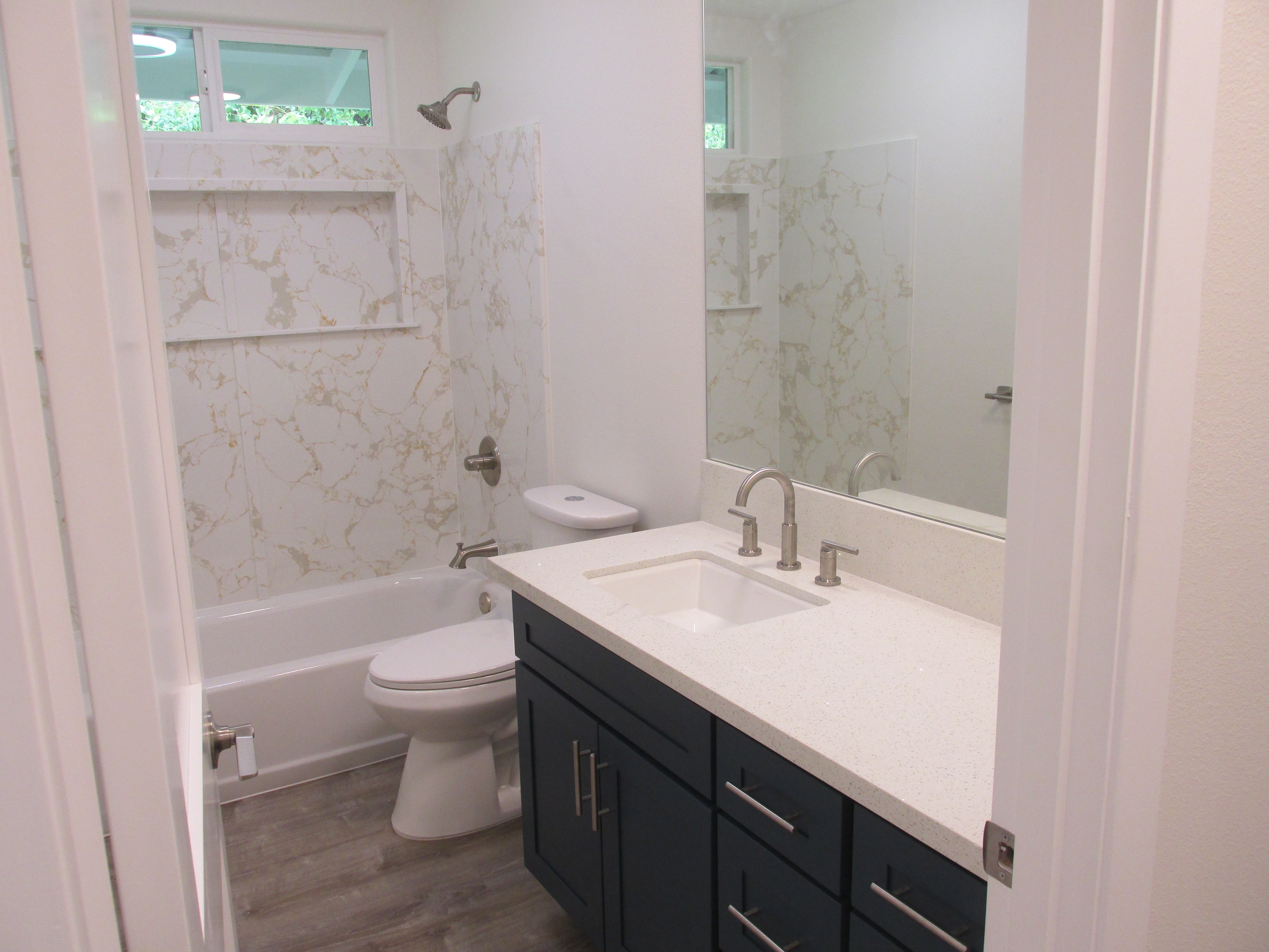 Bathroom with marble-pattern tub surround, high window, and dark vanity with white countertop.