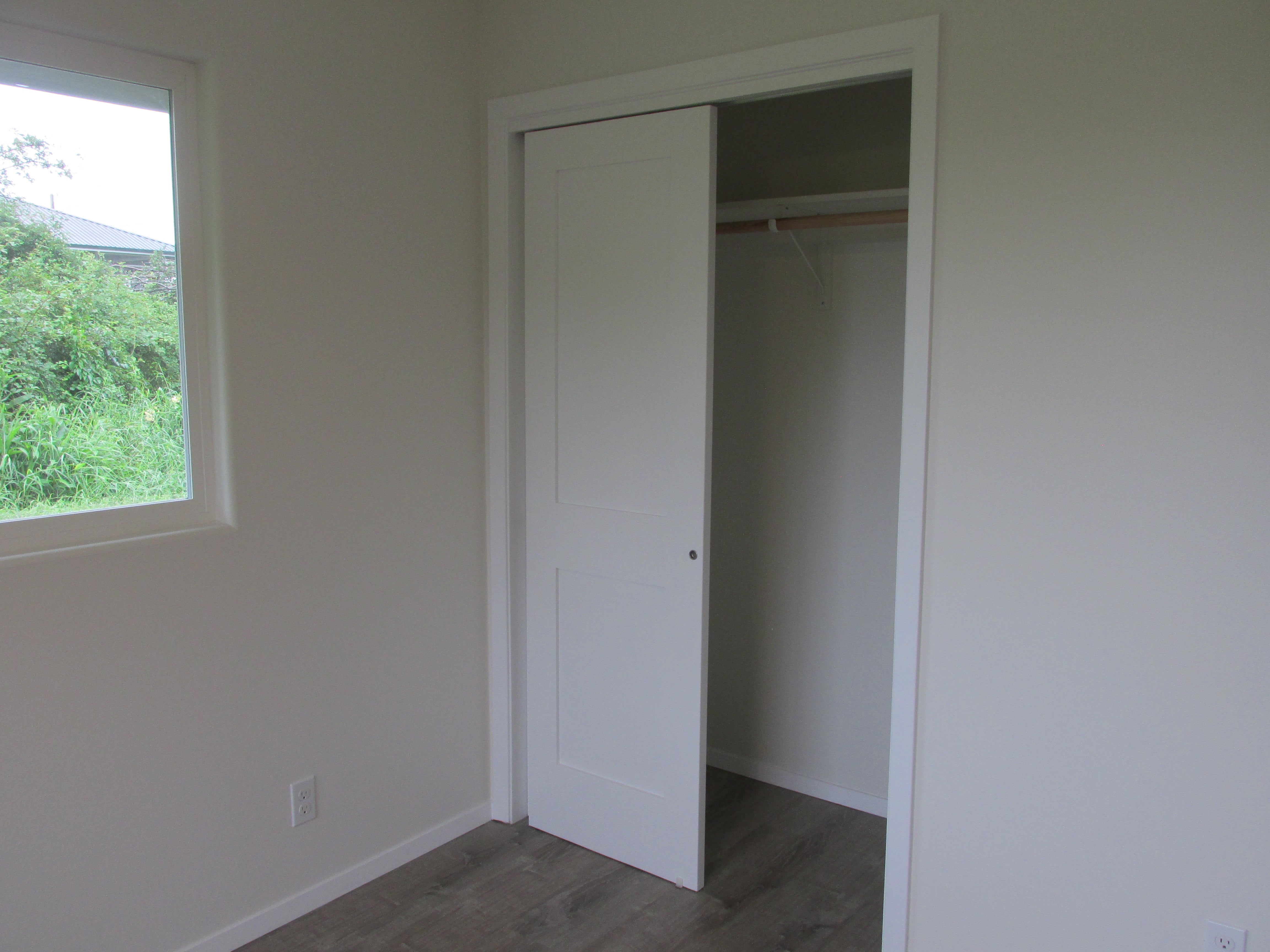 Empty room with gray flooring and an open closet beside a window overlooking greenery.