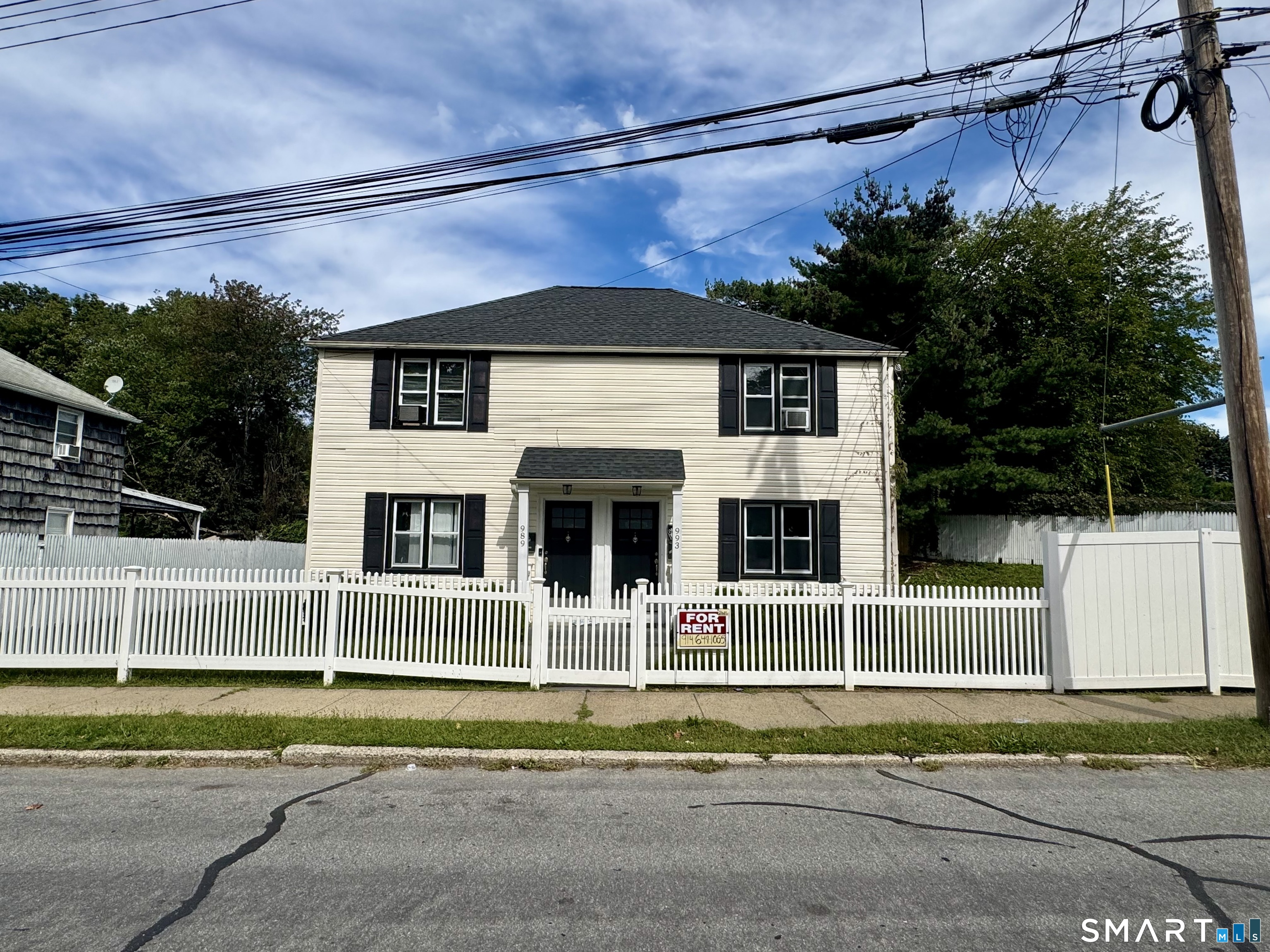 Cream duplex with twin black doors, white picket fence, and a For Rent sign.