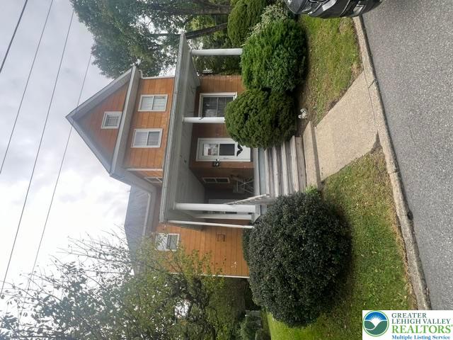 Two-story orange-brown house with a covered porch, white trim, front steps, and mature shrubs.