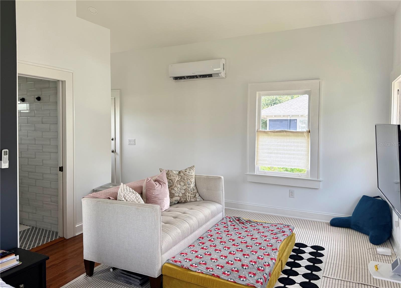Living room with a light sofa, patterned ottoman, striped rug, and adjacent tiled bathroom.