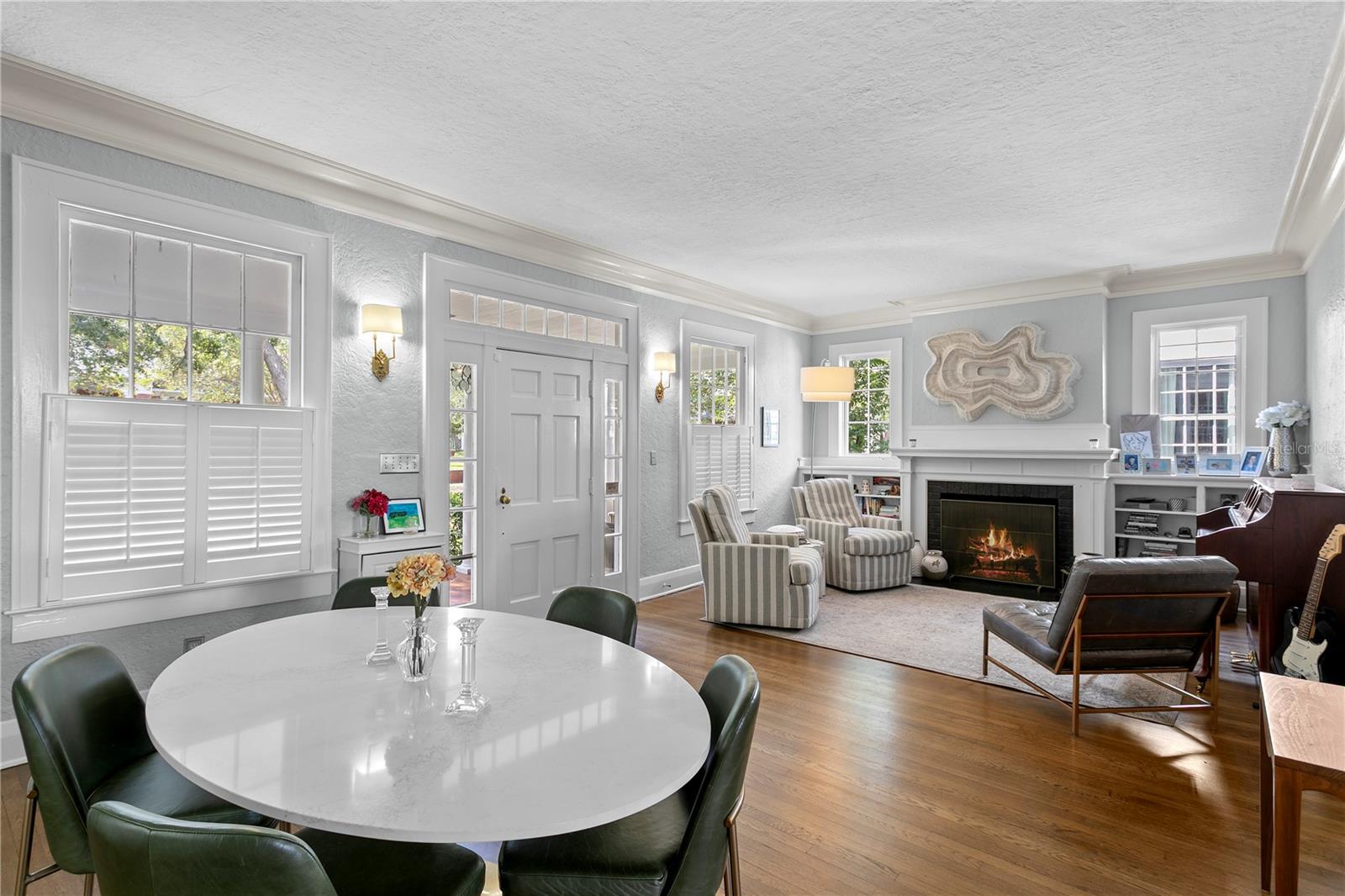 Furnished living and dining room with a white fireplace, striped chairs, and hardwood floors.