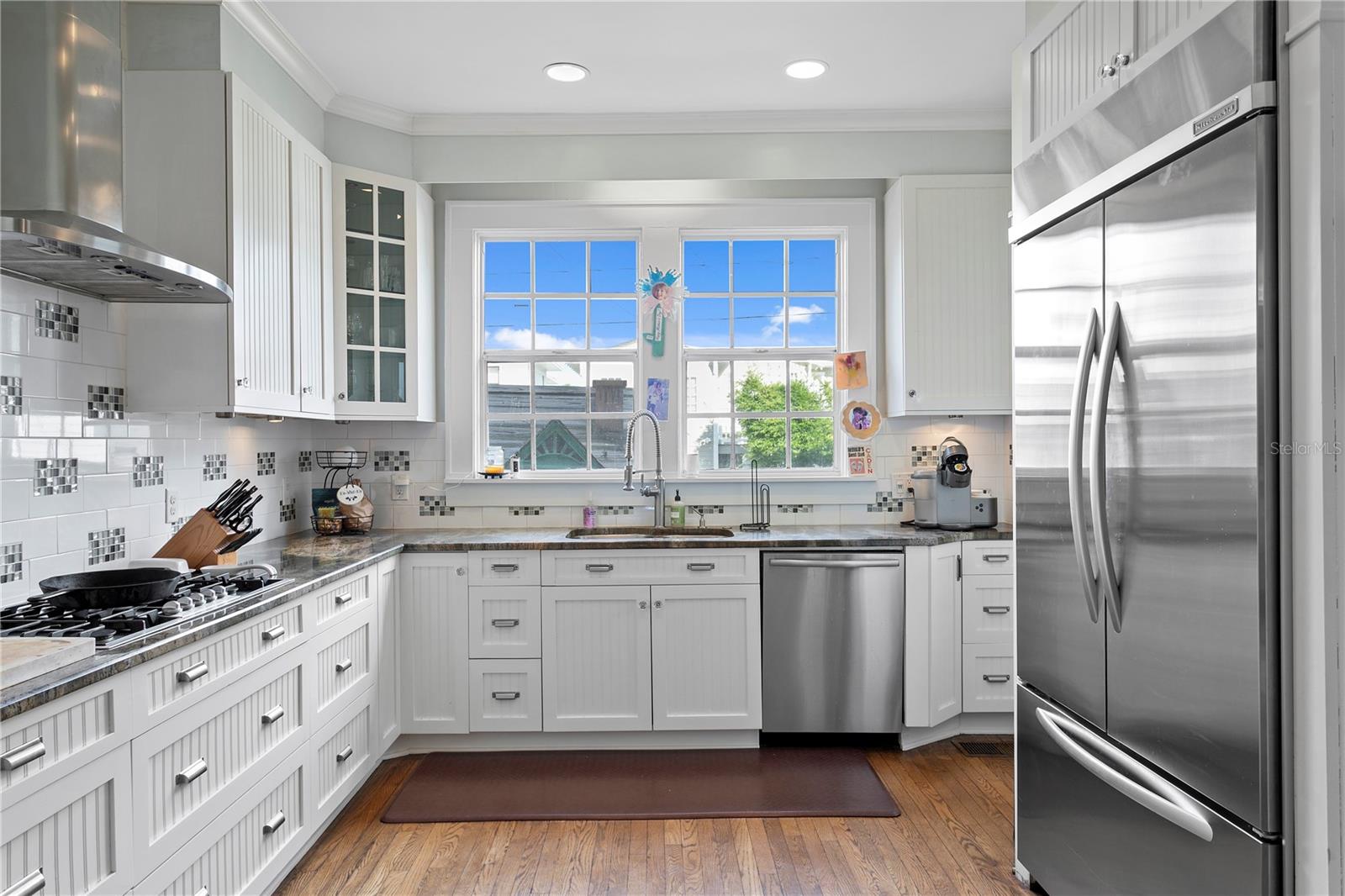 White kitchen with paneled cabinets, stainless-steel appliances, and a large window above the sink.