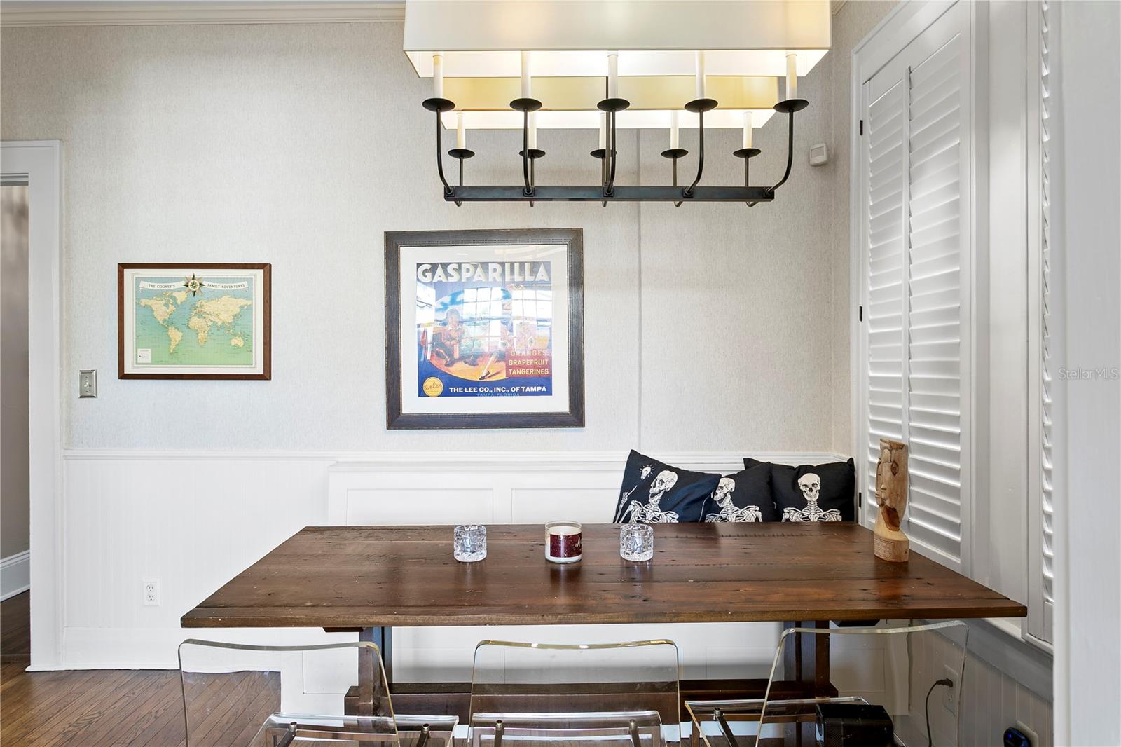 Dining nook with a dark wood table, built-in bench, skeleton-print pillows, and framed Gasparilla artwork.
