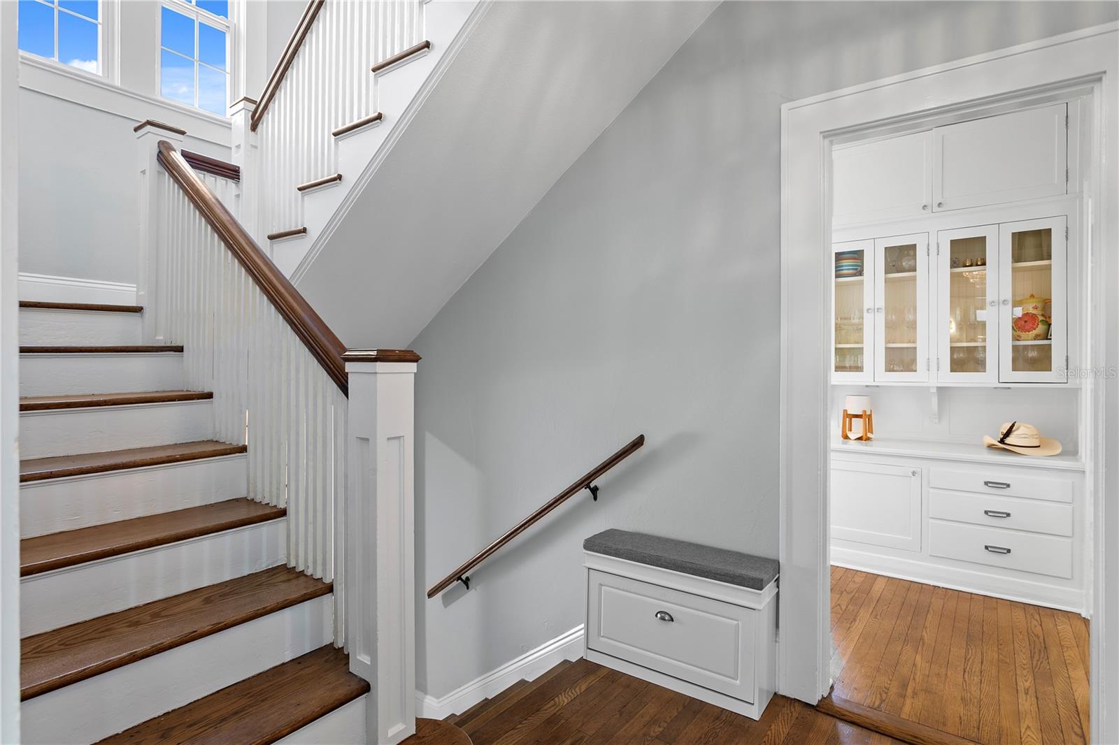 Interior staircase with dark wood treads and handrails beside a built-in glass-front cabinet.