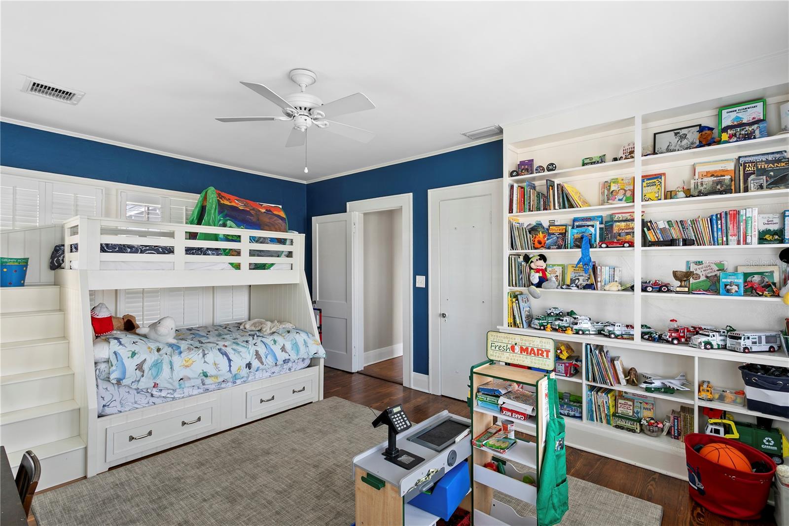 Child's bedroom with a white bunk bed, blue walls, and bookshelves filled with books and toys.