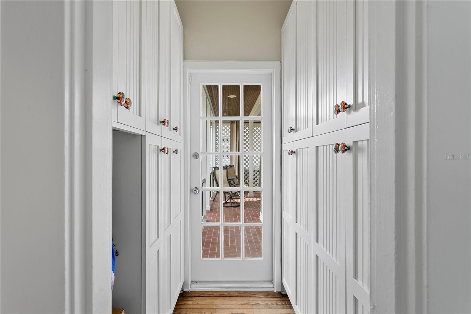 Entry hallway with white built-in cabinets and a glass-paneled door opening to a brick patio.