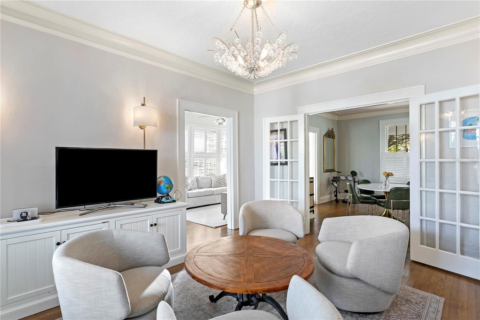 Living room with a crystal chandelier, round wood coffee table, and open French doors to the dining room.