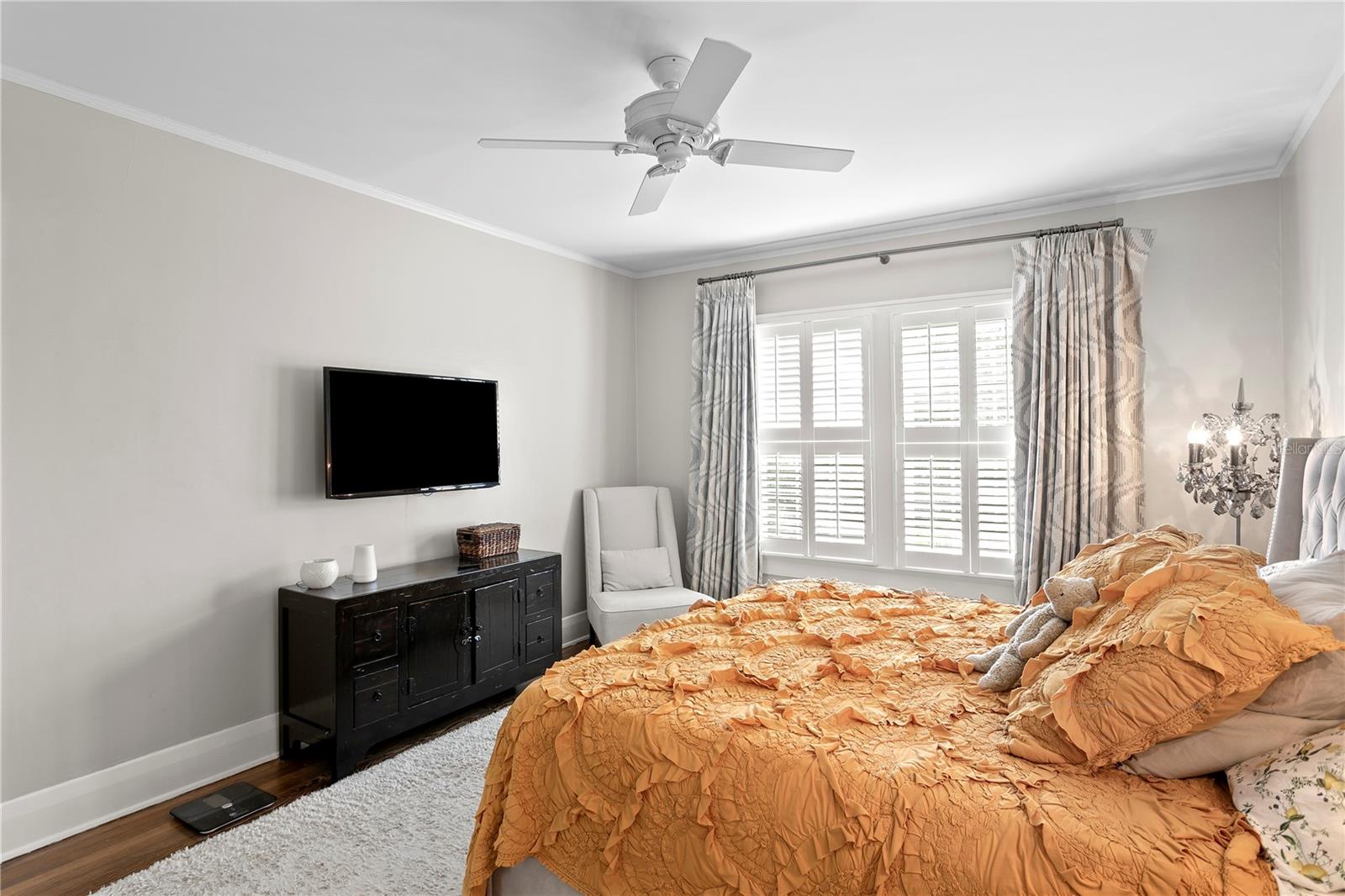 Bedroom with an orange ruffled bedspread, plantation shutters, and dark wood media console.