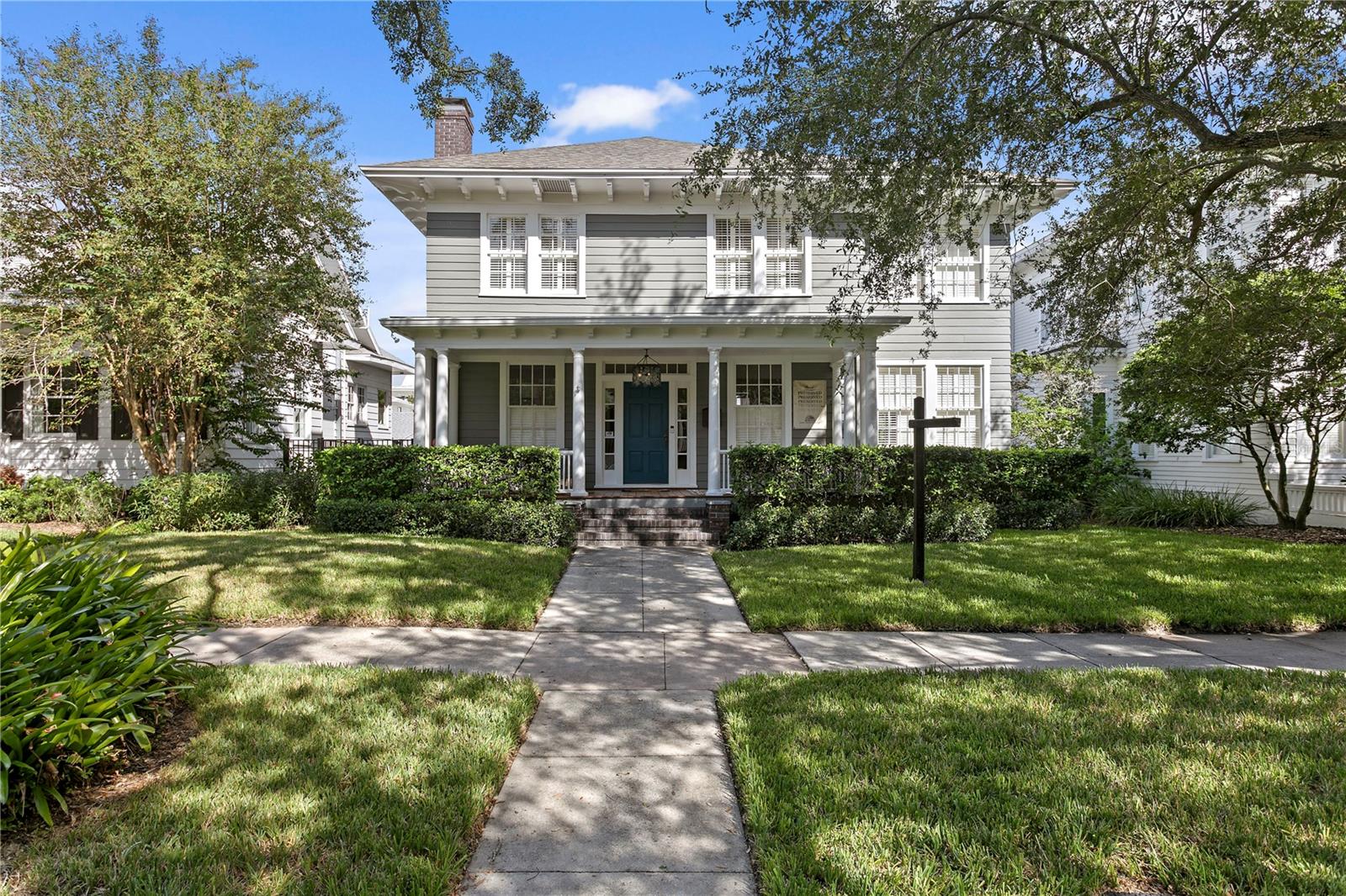 Two-story gray house with a columned porch, blue front door, and walkway through the lawn.