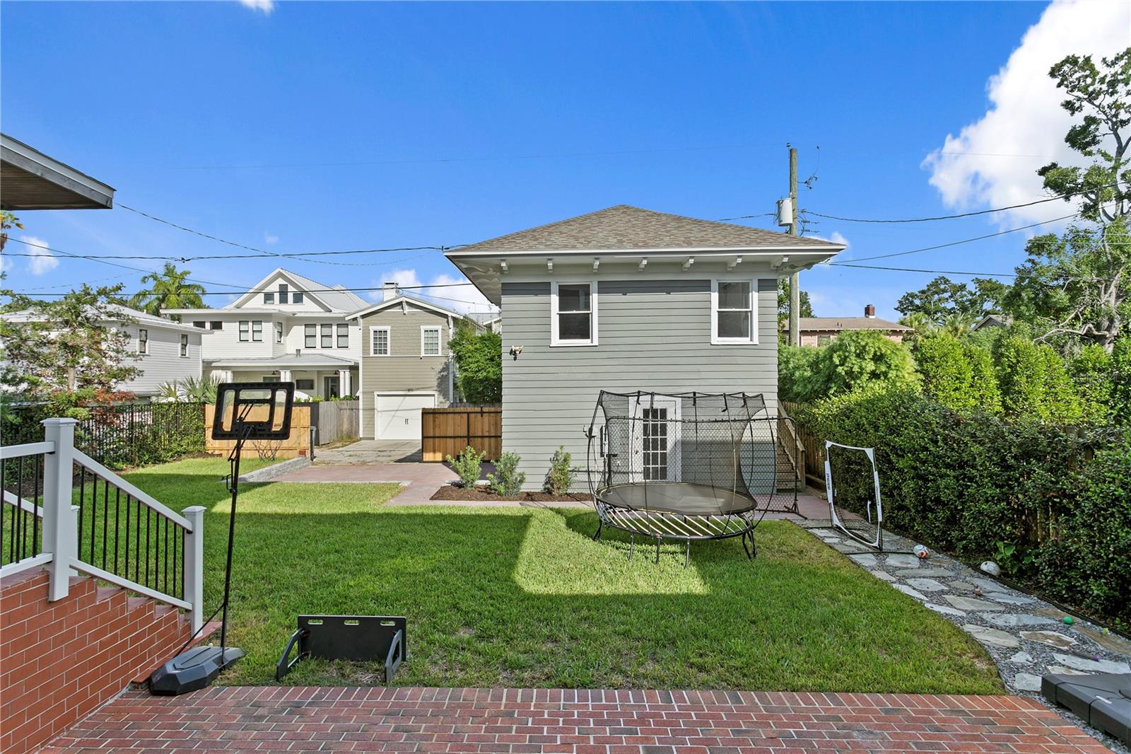 Backyard with a broad lawn, brick patio, trampoline, and gray-sided house.