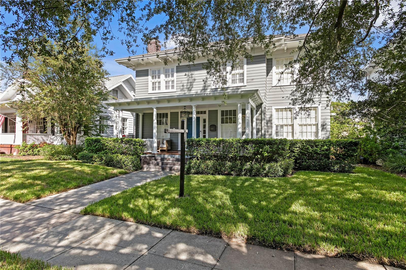 Two-story gray house with a columned white porch, front hedges, and a shaded lawn.
