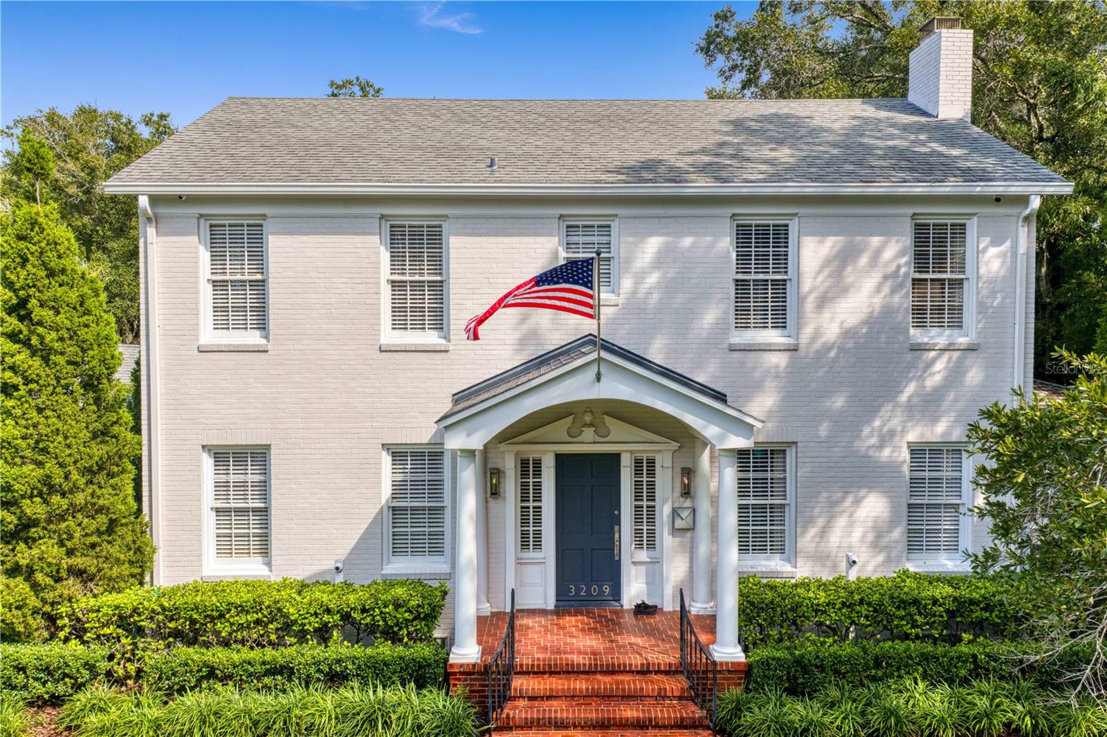White two-story brick home with a columned entry, brick steps, and an American flag.